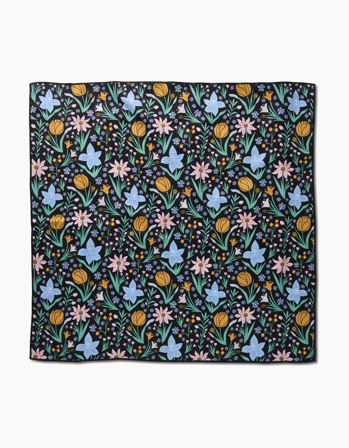 The Garden of Light by Danelys Sidron is a square fabric with a black background and a repeating pattern of colorful yellow, pink, and blue flowers with green leaves, made from highly absorbent post-consumer recycled materials.