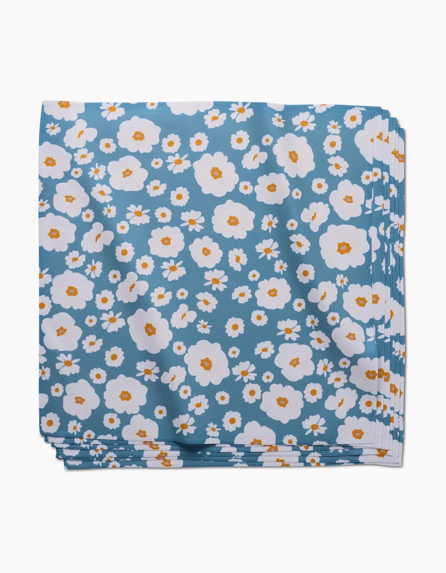 The GEOMETRY Happy Daysies Dinner Napkin Set is folded, made from Geosuede fabric, and features a blue background with white and orange flower patterns.