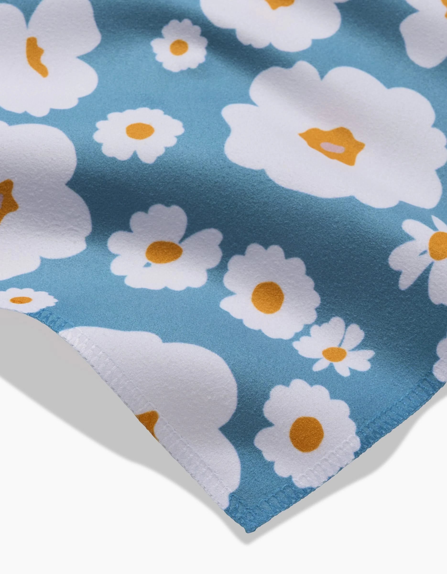 A close-up of GEOMETRYs Happy Daysies features blue Geosuede fabric with white and yellow daisy prints, neat stitching, and a soft texture—ideal for a stylish dinner napkin set made from recycled materials.