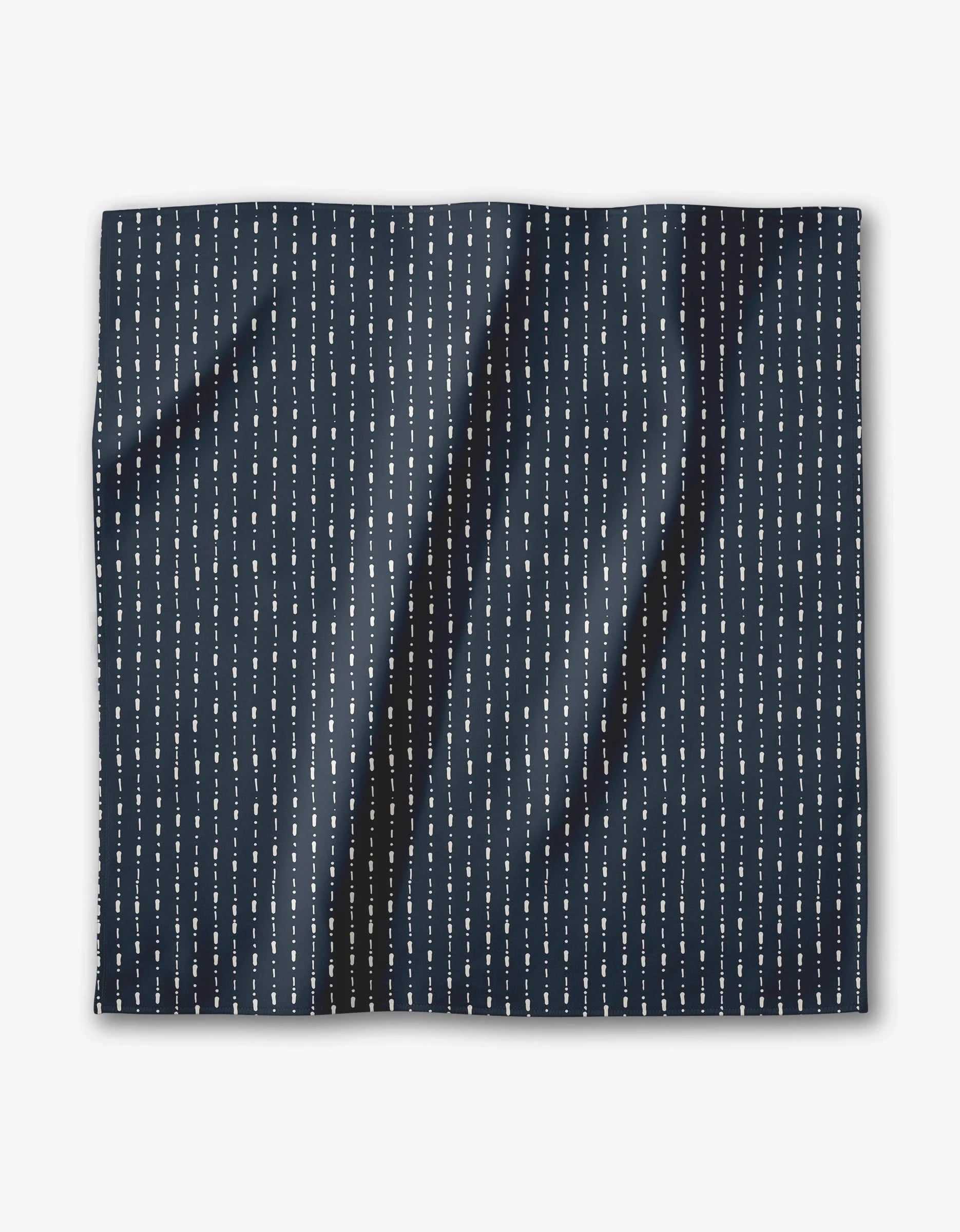 The Kealia dinner napkin set by GEOMETRY features dark navy blue Geosuede fabric made from recycled materials, with vertical white dashed lines in a minimalist repeat. The napkins are square and have a slightly creased appearance.