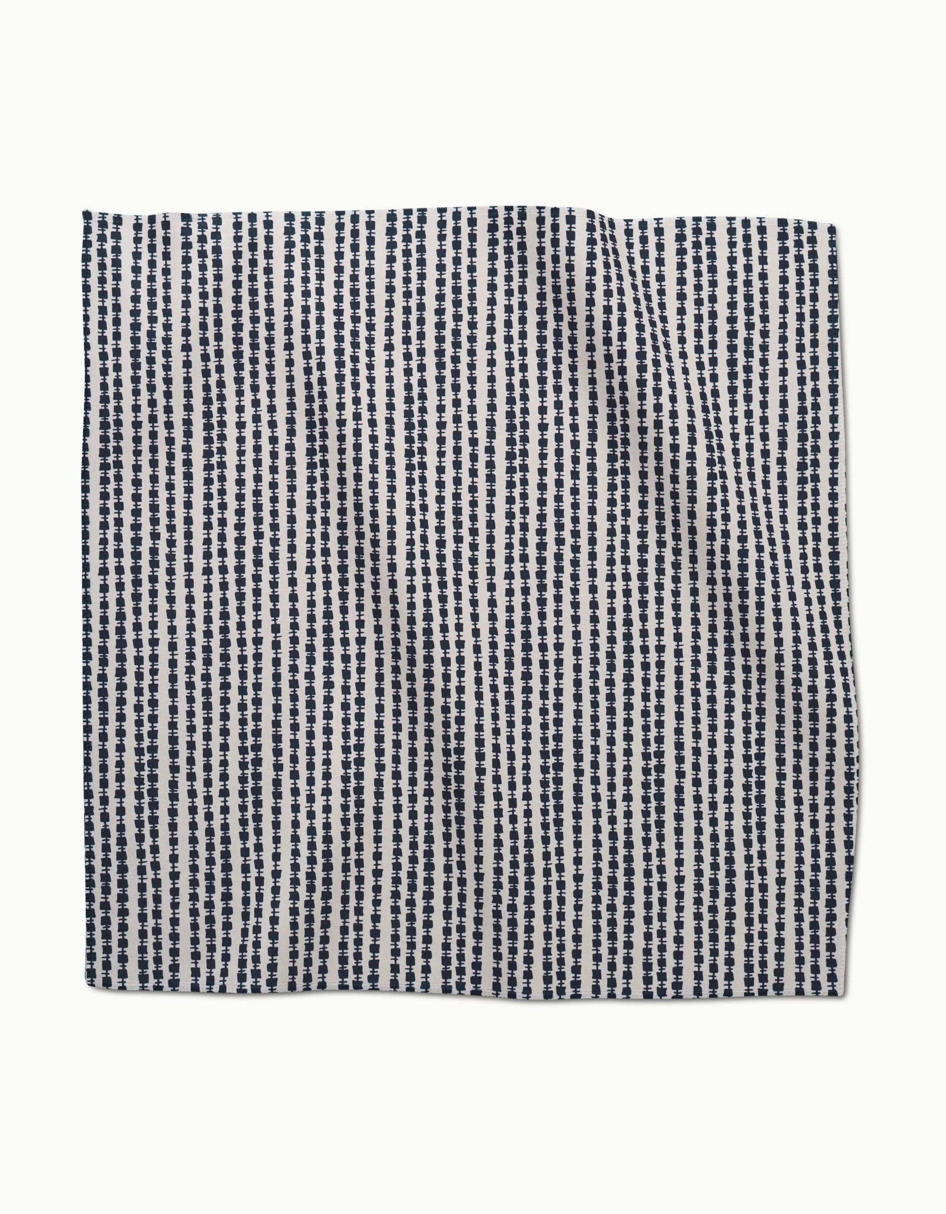 The Kealia dinner napkin set by GEOMETRY is made from Geosuede fabric with vertical navy blue dotted lines on white—slightly wrinkled and photographed against a plain backdrop.