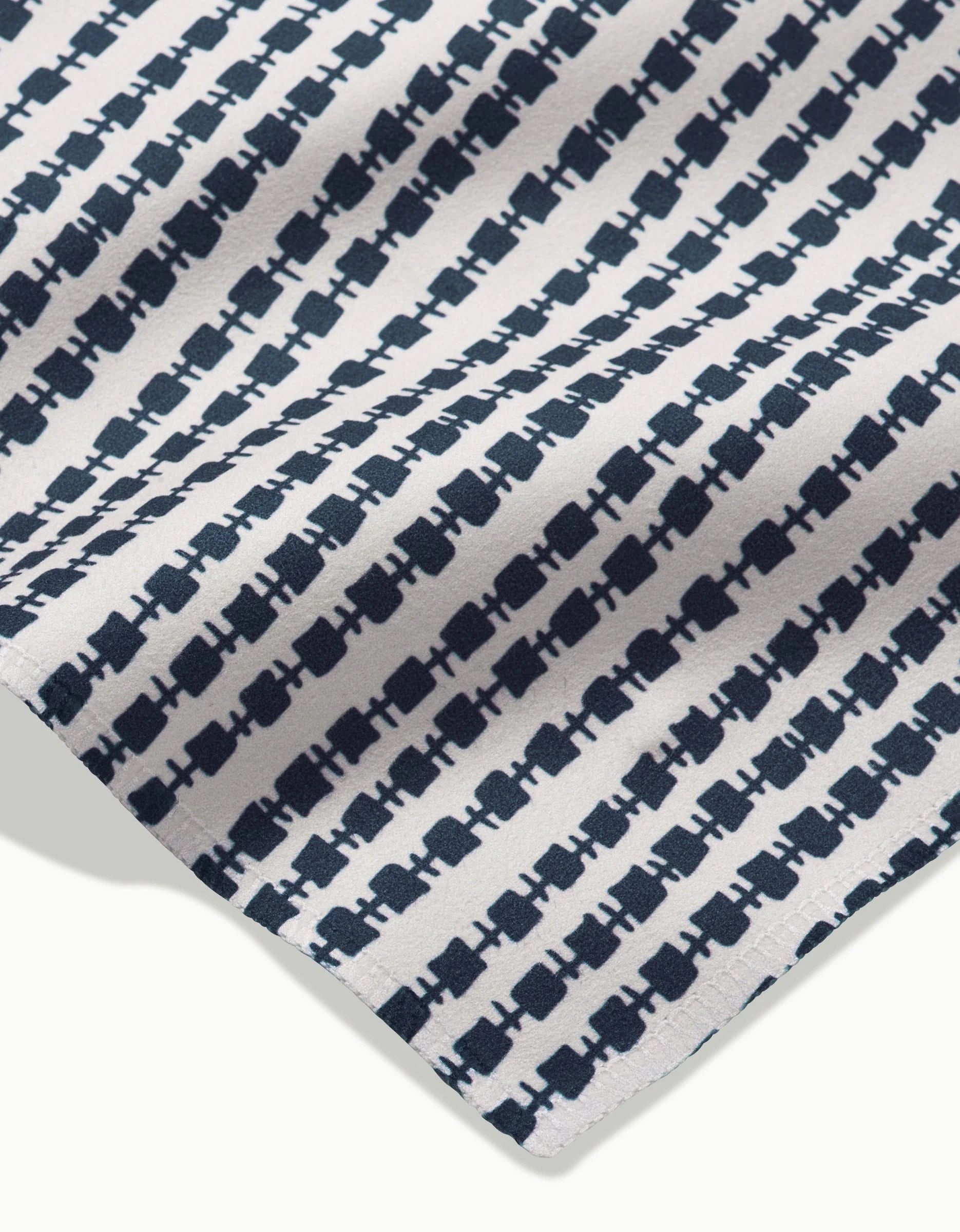 A close-up of Kealia by GEOMETRY shows white Geosuede fabric with evenly spaced navy abstract geometric rows. Made from recycled materials, the fabric has a slight fold at the bottom corner.