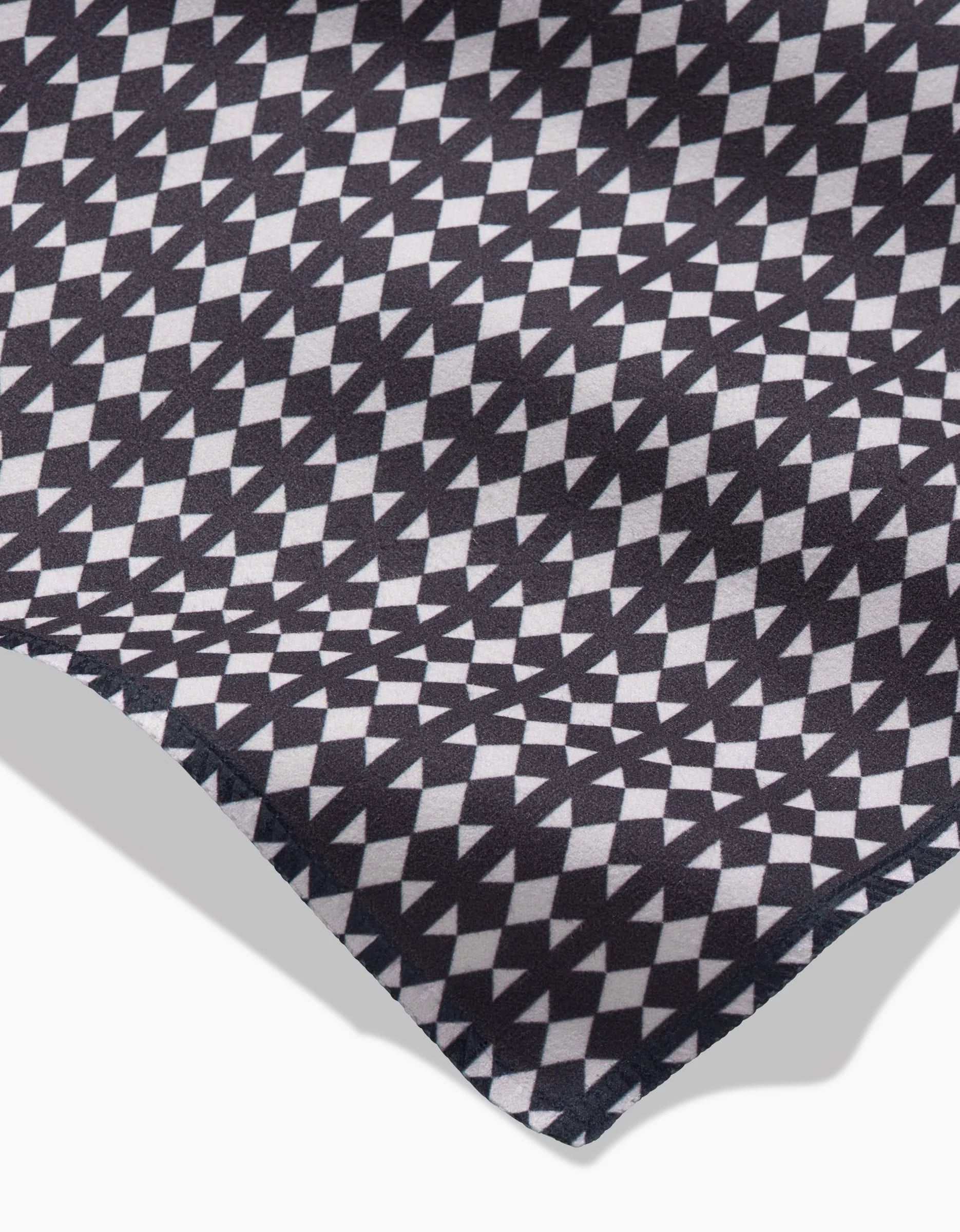 A close-up of GEOMETRY’s Maori fabric showcases black and white geometric patterns of triangles and diamonds, with a subtle fold—perfect for eco-friendly dinner napkins made from recycled materials.