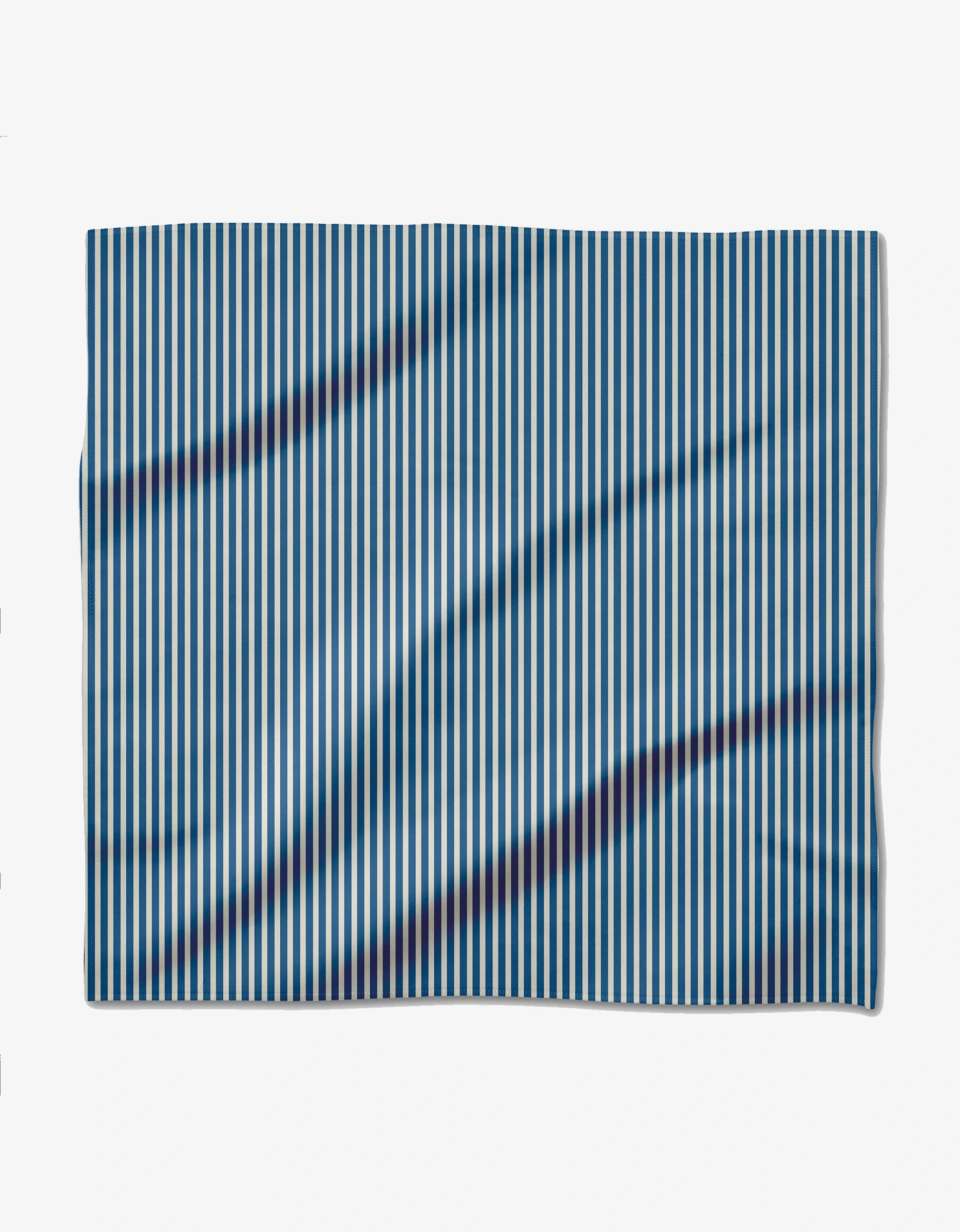 The Seafaring Dinner Napkin by GEOMETRY, made from recycled Geosuede fabric, displays vertical blue and white stripes. Its rectangular shape shows gentle folds and subtle shadows against a plain white background.