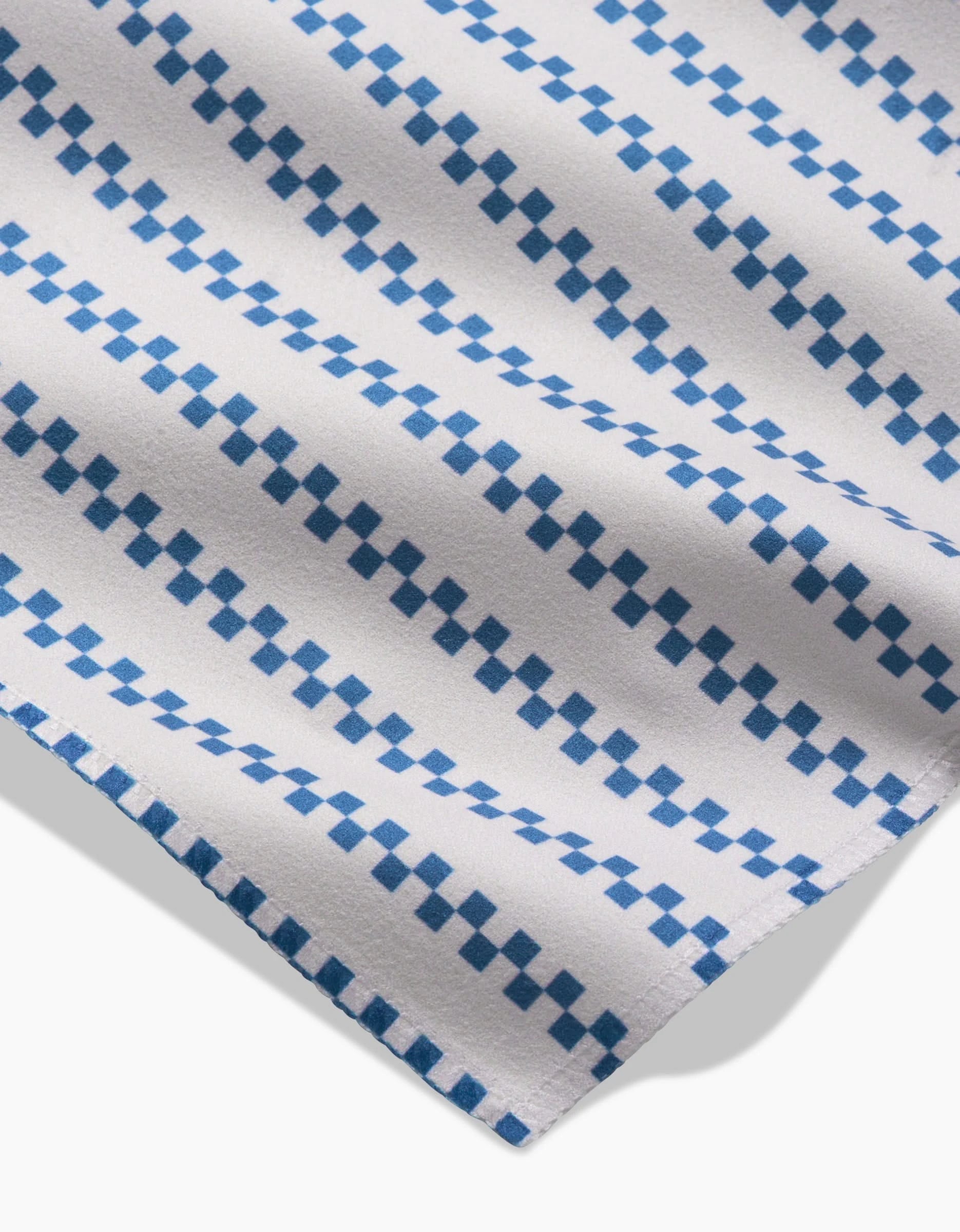 The Seafaring fabric by GEOMETRY features white Geosuede made from recycled materials, with diagonal rows of blue squares and rectangles in a geometric pattern, shown at an angle with a soft shadow below.