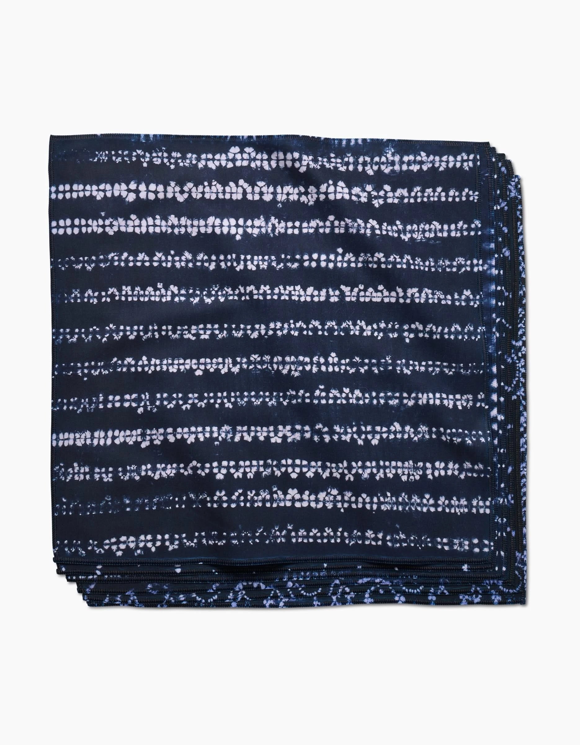 A neatly folded Shibo dinner napkin by GEOMETRY, made of dark blue Geosuede fabric with a white horizontal dotted tie-dye pattern, displayed on a white background.