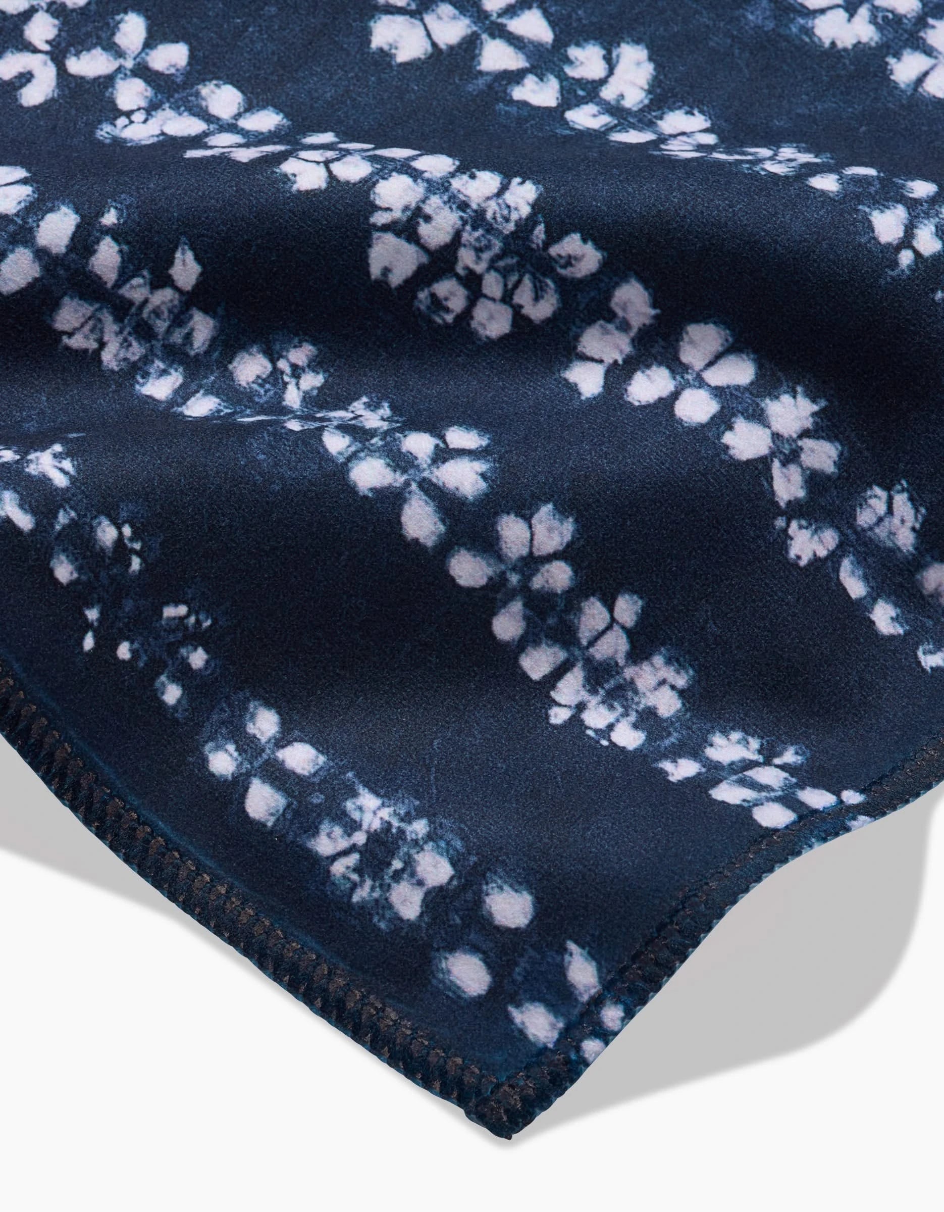 A close-up of GEOMETRYs Shibo, a soft dark blue Geosuede fabric featuring a white batik-style floral pattern and visible edge stitching—perfect for an eco-friendly, recycled Dinner Napkin Set.