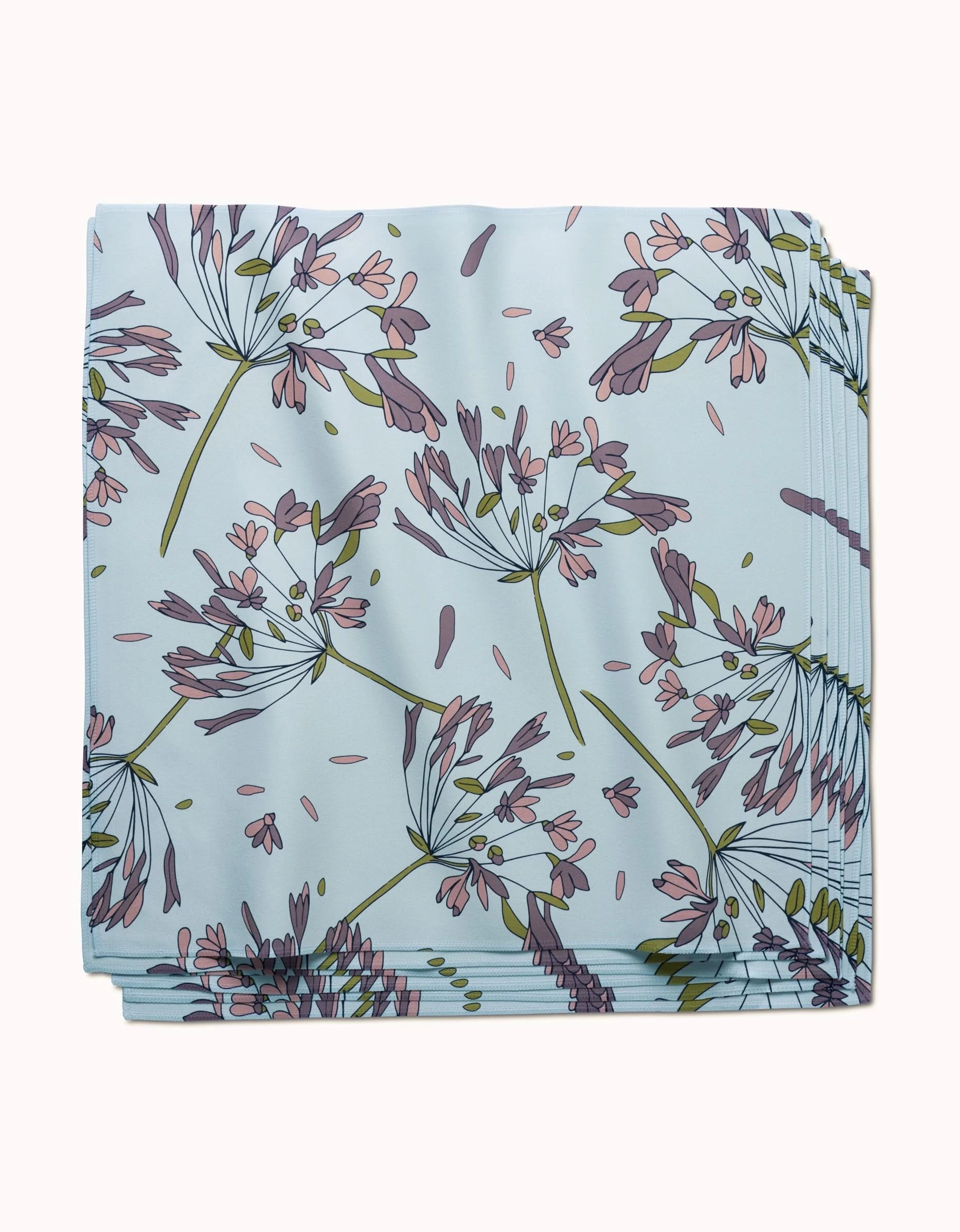 The Wind by GEOMETRY: a folded, light blue reusable dinner napkin with a botanical print of delicate purple, pink, and green flowers and leaves.