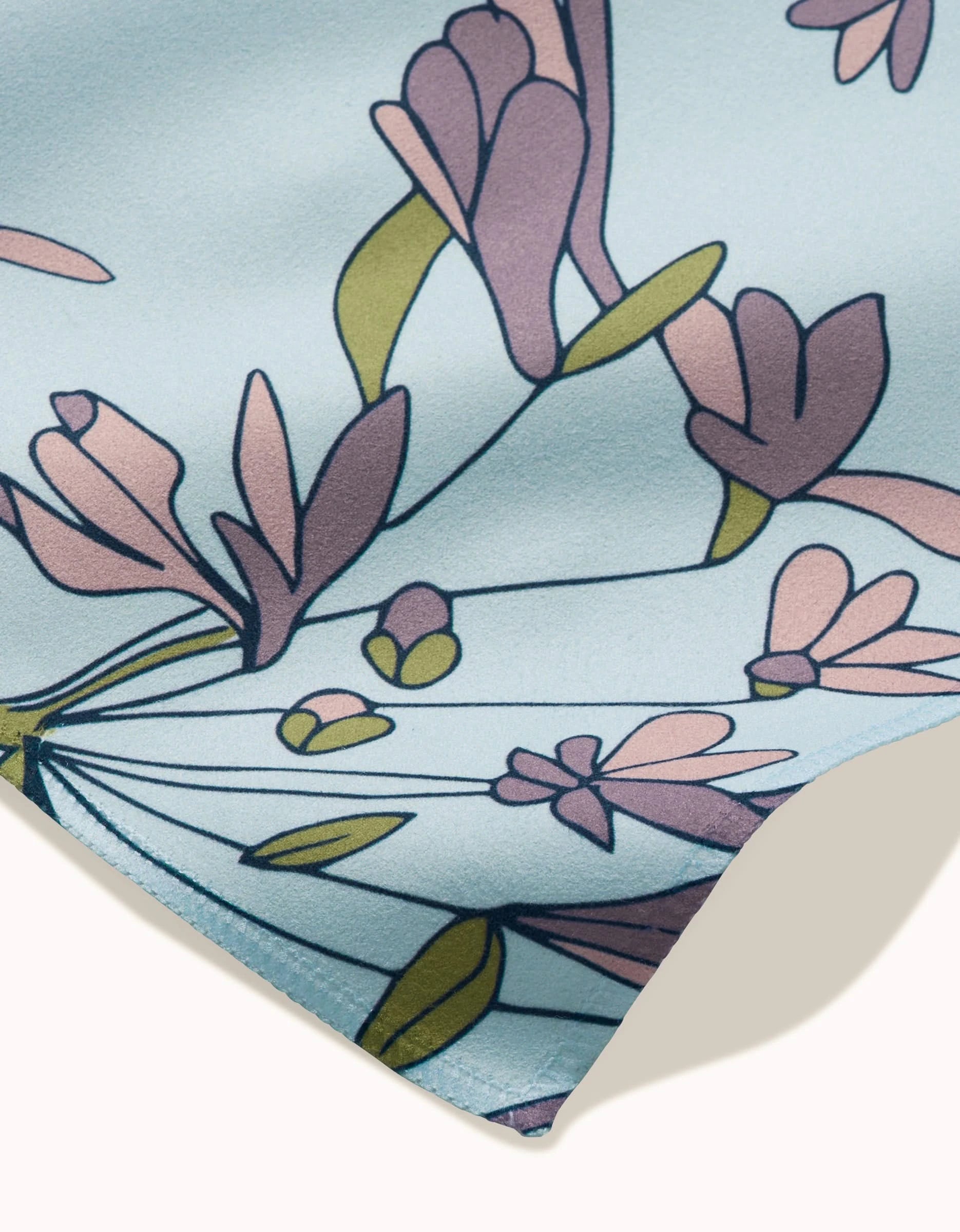 A close-up of The Wind dinner napkin set by GEOMETRY, showing soft light blue fabric with pink and purple flowers, green stems and leaves, and neatly finished edges. Reusable, smooth, and stylish for any table.