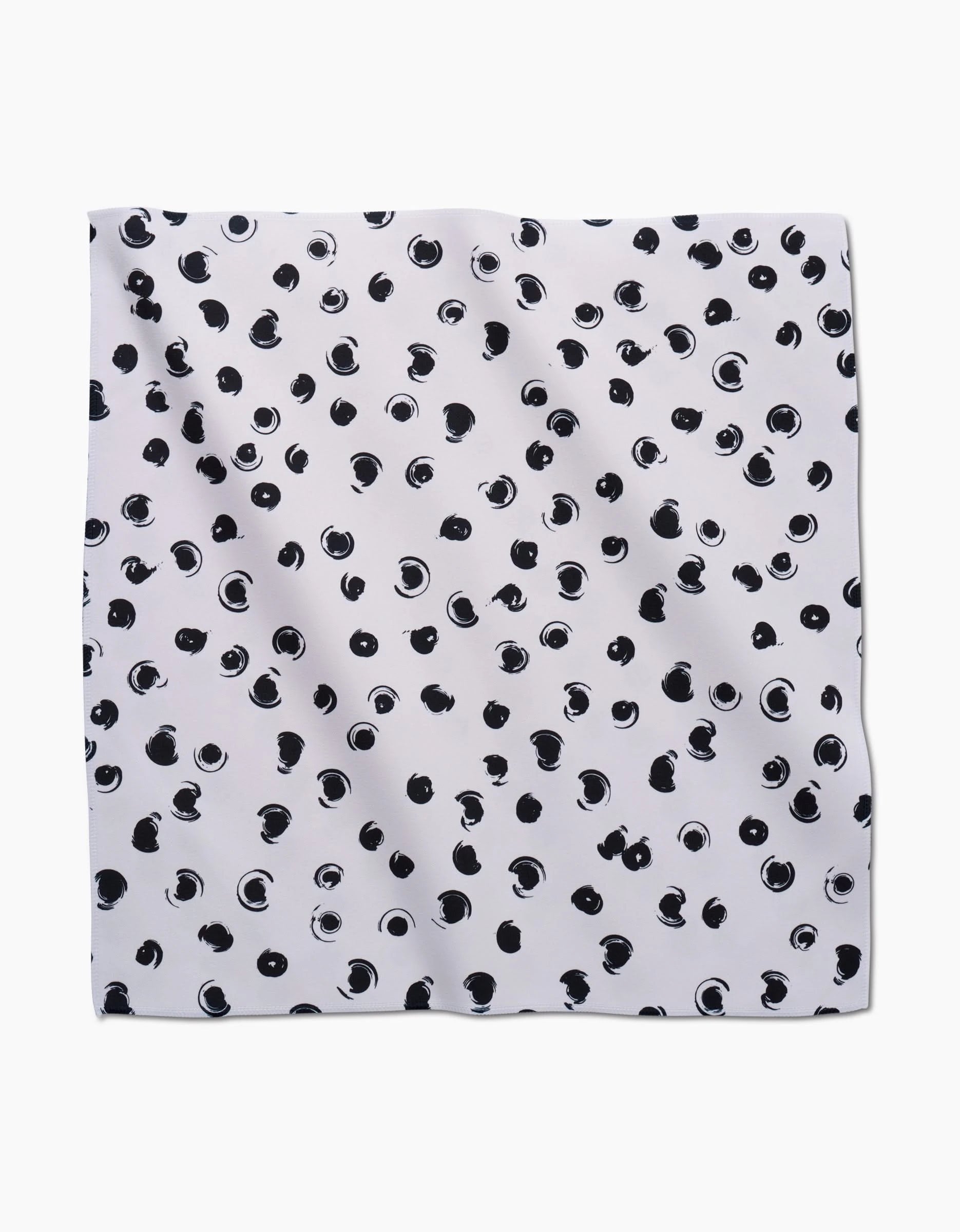 The Tiny Drops Dinner Napkin Set by GEOMETRY features soft white Geosuede fabric, adorned with scattered black abstract dots and circular brushstrokes, and is shown flat on a white background.