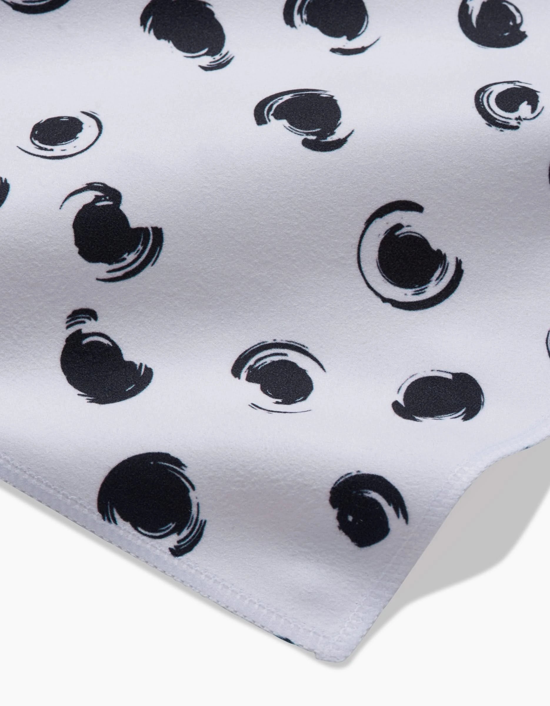 A close-up of the GEOMETRY Tiny Drops dinner napkin set, made from recycled Geosuede fabric, showcases an abstract black circular pattern on white with visible stitched edges.