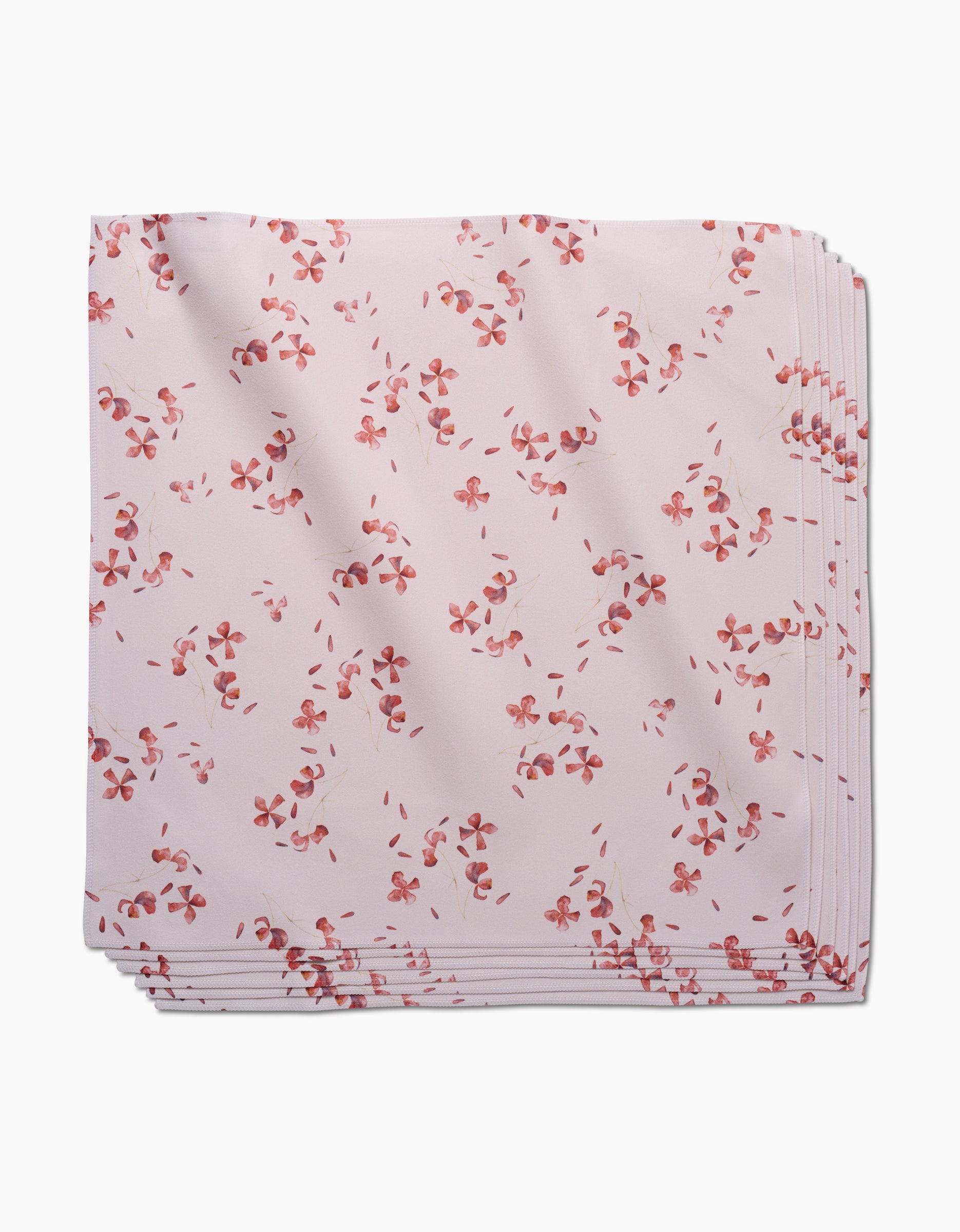 The Tiny Petals dinner napkin by GEOMETRY features folded pale pink Geosuede fabric with a pattern of small red and pink flowers, displayed on a white background.