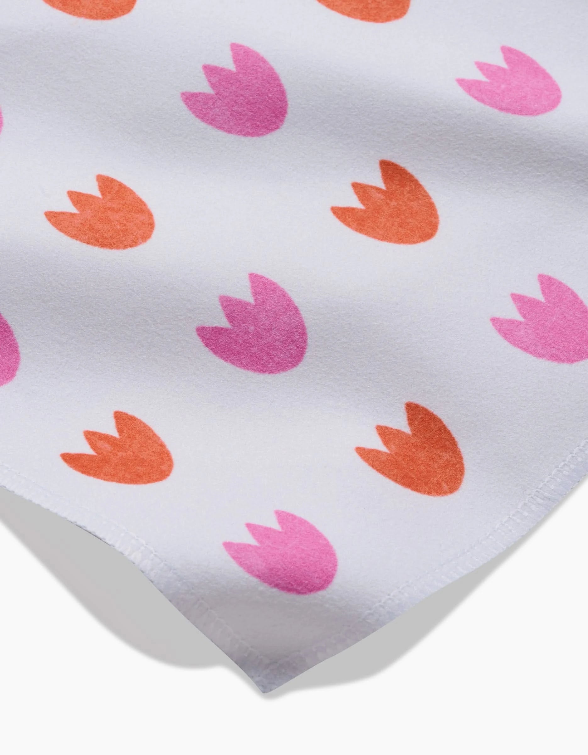 A close-up of the Addison dinner napkin set by Amy MacCready, made from white Geosuede fabric with pink and orange abstract tulips, recycled materials for a soft feel, and a slightly curved bottom edge.