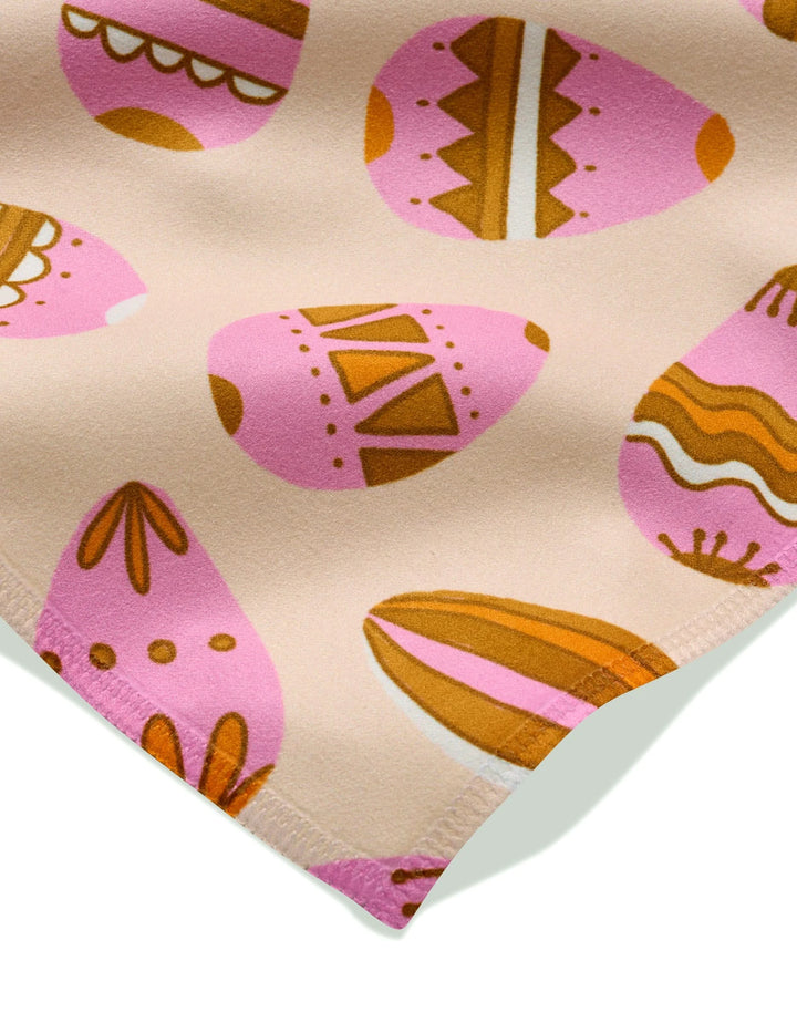 A close-up of the Arledge dinner napkin set by Amy MacCready, crafted from eco-friendly recycled fabric and featuring pink and orange Easter eggs with geometric and wavy designs on a light beige background.