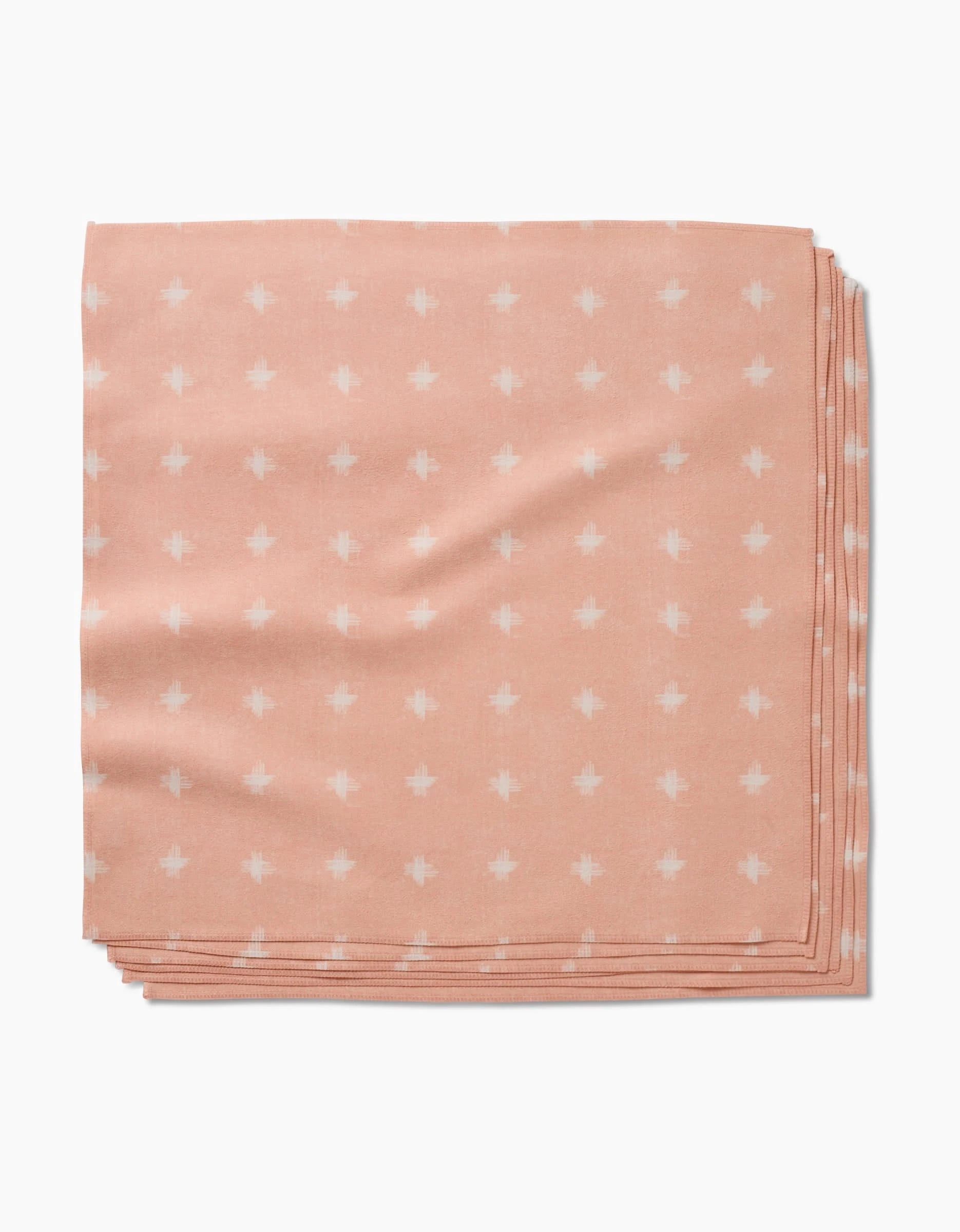 The Aveline dinner napkin by Amy MacCready is a peach Geosuede cloth with a white geometric dot pattern, made from post-consumer recycled materials. It’s shown folded against a plain white background.