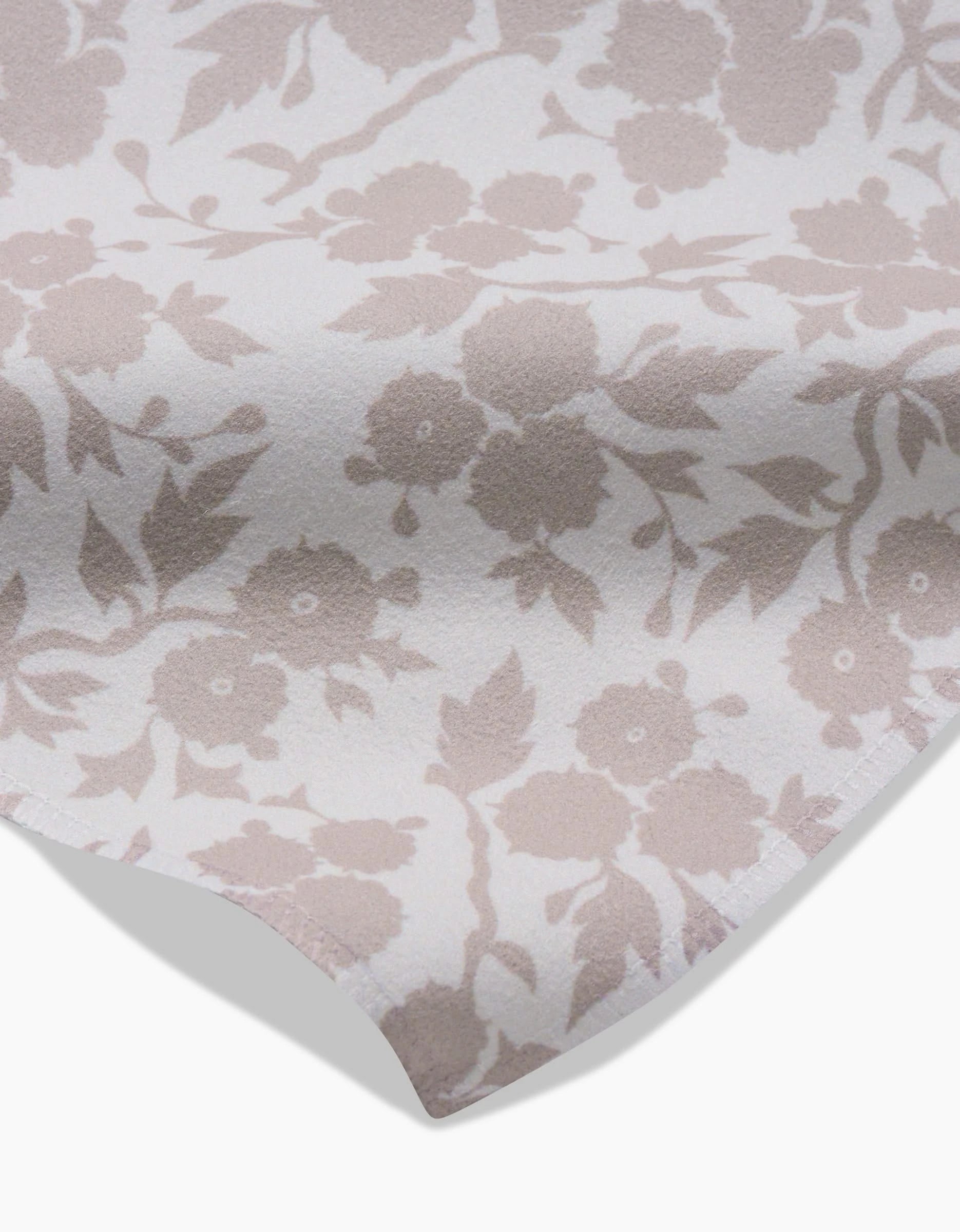 A close-up of GEOMETRYs Bettys Buds Geosuede fabric, made from recycled materials, shows a light beige floral pattern on white. The slightly folded fabric reveals its soft texture and elegant floral details.
