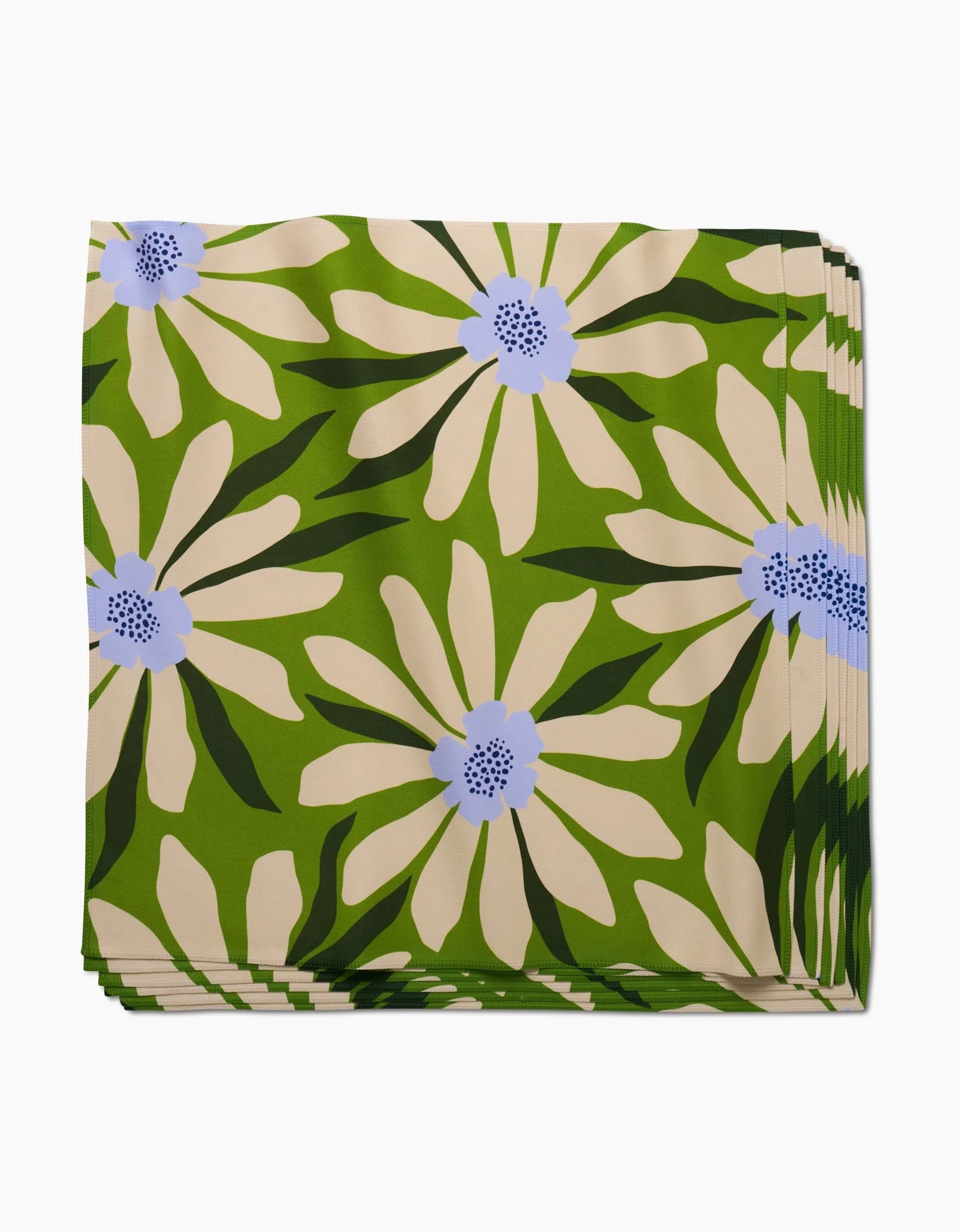 A stack of GEOMETRY’s Bliss and Bloom dinner napkins in Geosuede fabric, featuring a bold green floral pattern with large cream flowers, light blue centers, and dark green leaves.