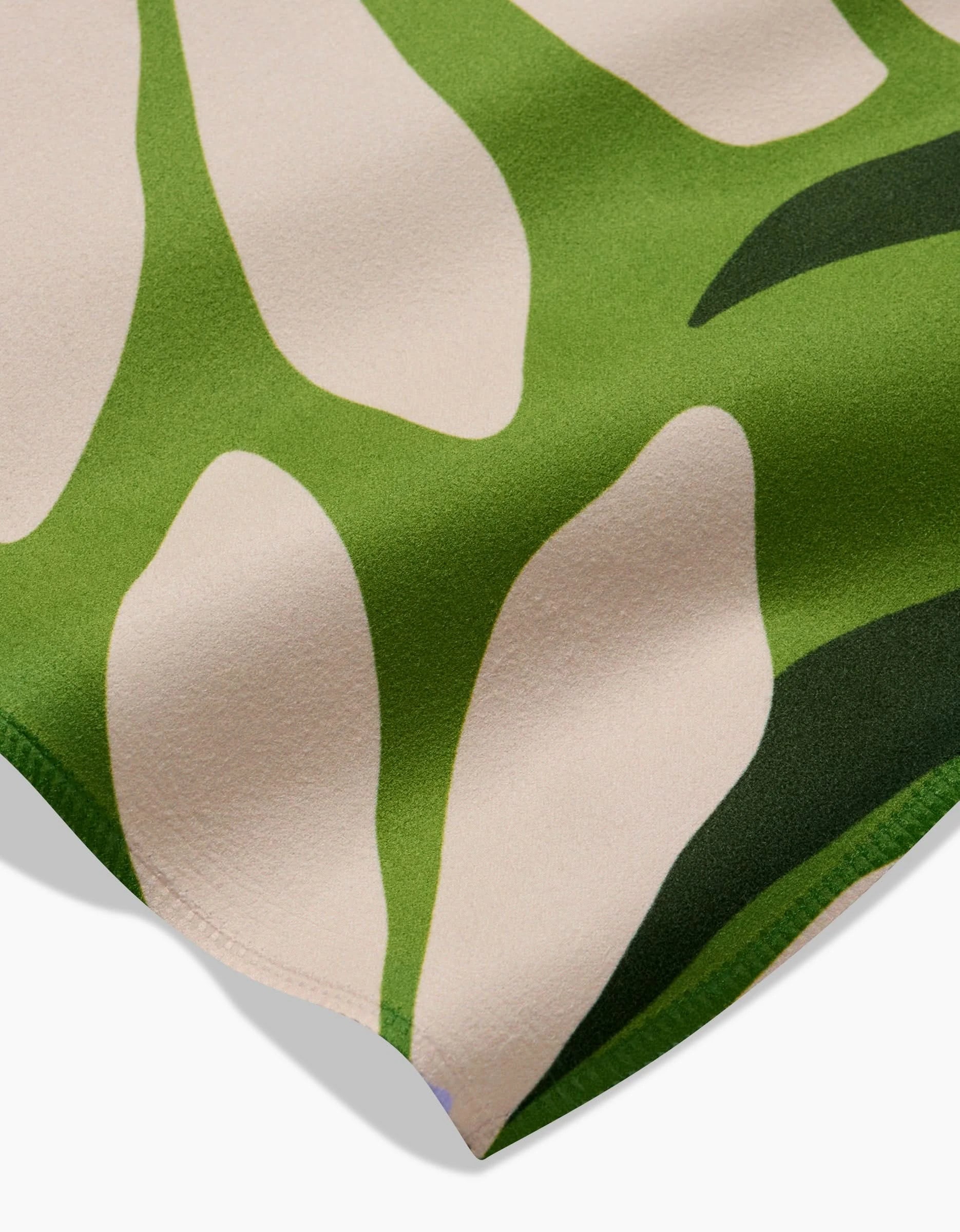 Close-up of the Bliss and Bloom Geosuede fabric by GEOMETRY, featuring an abstract pattern with cream shapes edged in green. The soft, smooth material evokes leaf-like forms—ideal for creating elegant dinner napkins.