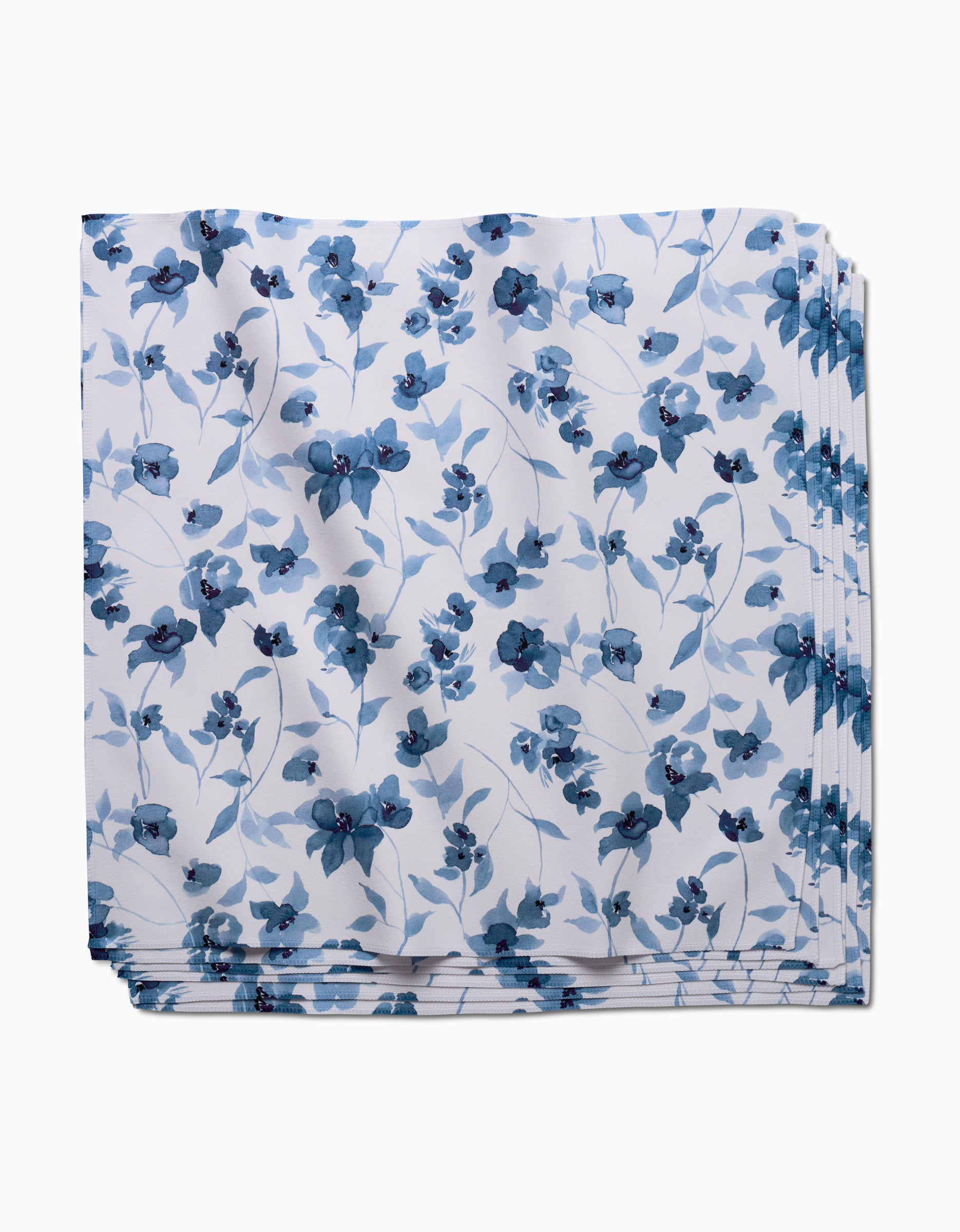 The Aubrey Fairchild Blue Floral is a square dinner napkin made from soft, recycled Geosuede fabric, featuring a white background with blue flowers and leaves. The napkin arrives neatly folded.