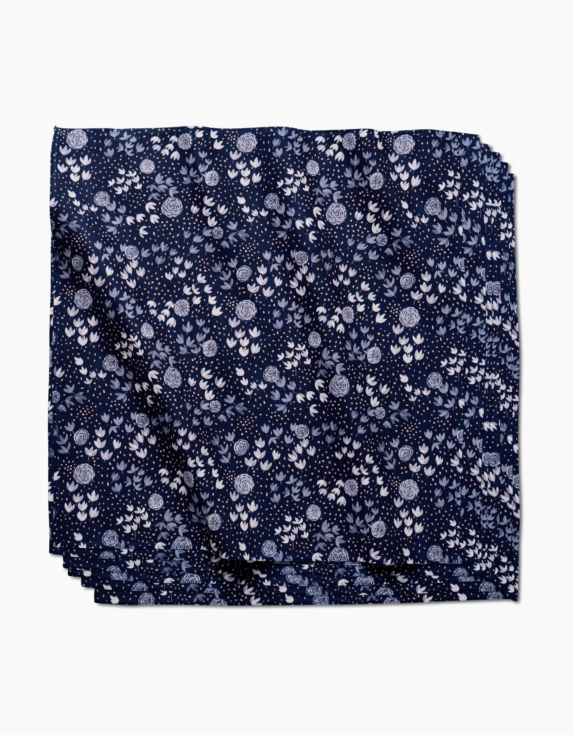 Blue Winter Petal by Katie OShea is a navy Geosuede fabric square with an intricate pattern of white and light blue floral motifs—perfect as a recycled dinner napkin, shown here against a white background.