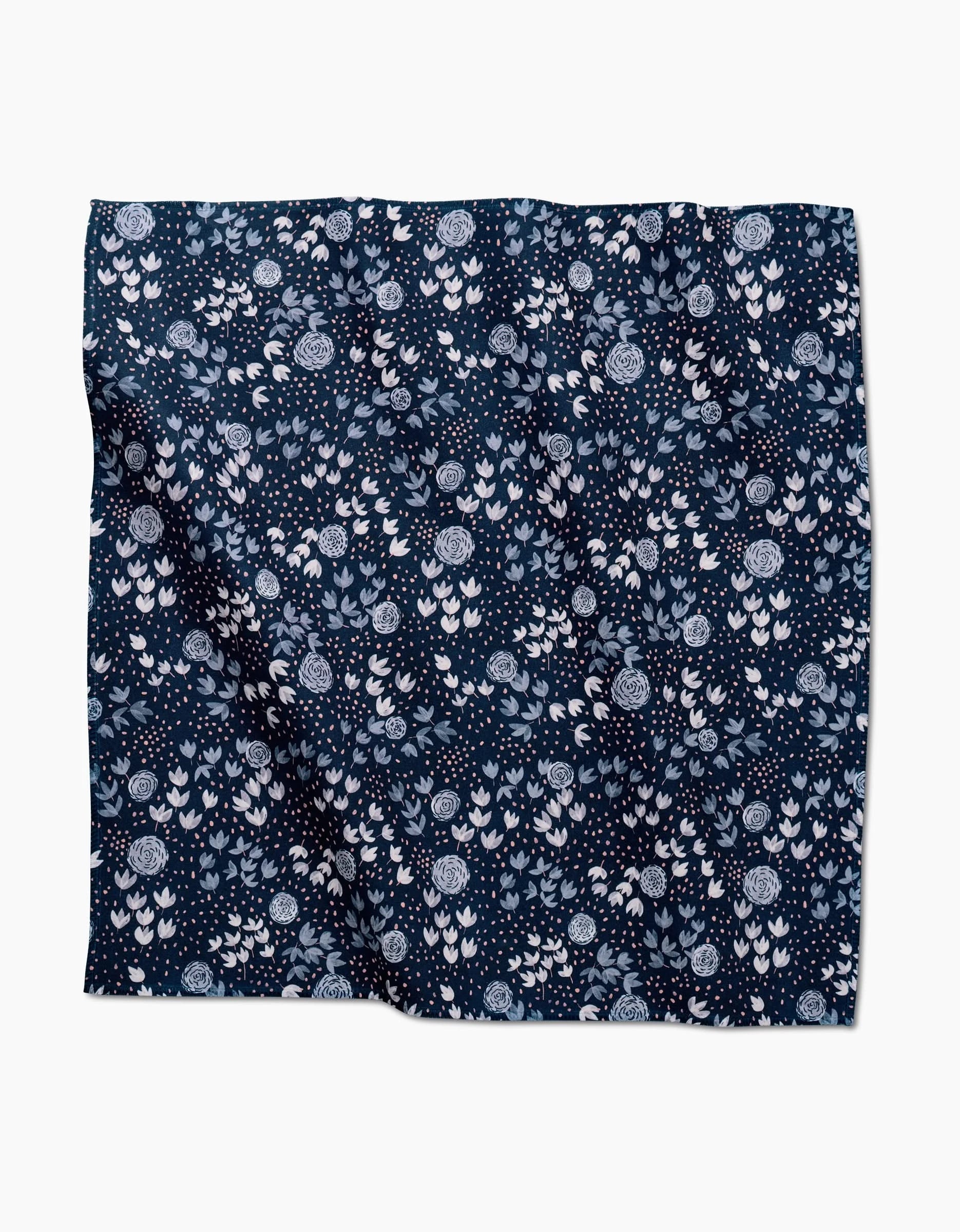 The Blue Winter Petal dinner napkin by Katie OShea features a dense white and light blue floral pattern on navy blue Geosuede—an elegant accent for any table setting.
