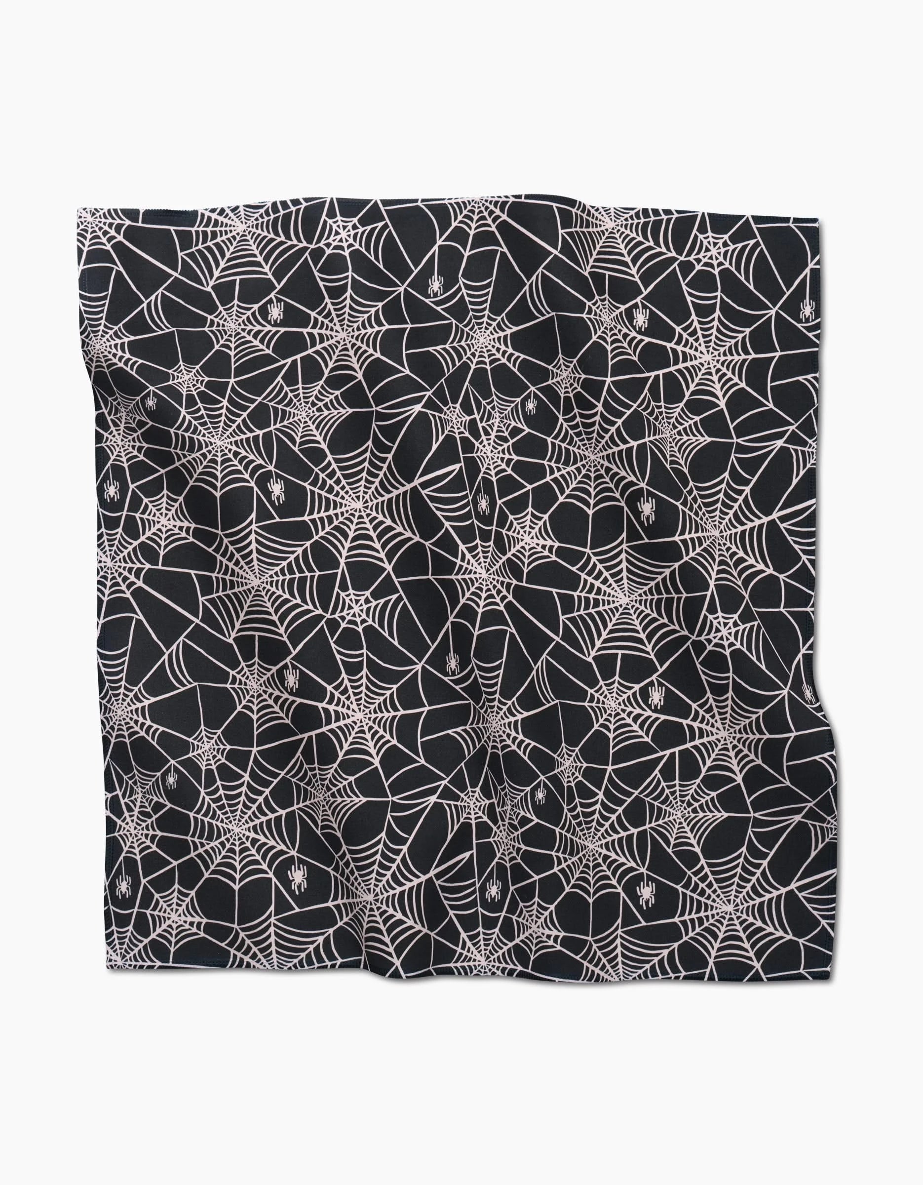 The Kayla Ann Booos napkin is a square, eco-friendly black fabric featuring white spider webs and small spiders. Slightly wrinkled, it’s displayed on a white background.
