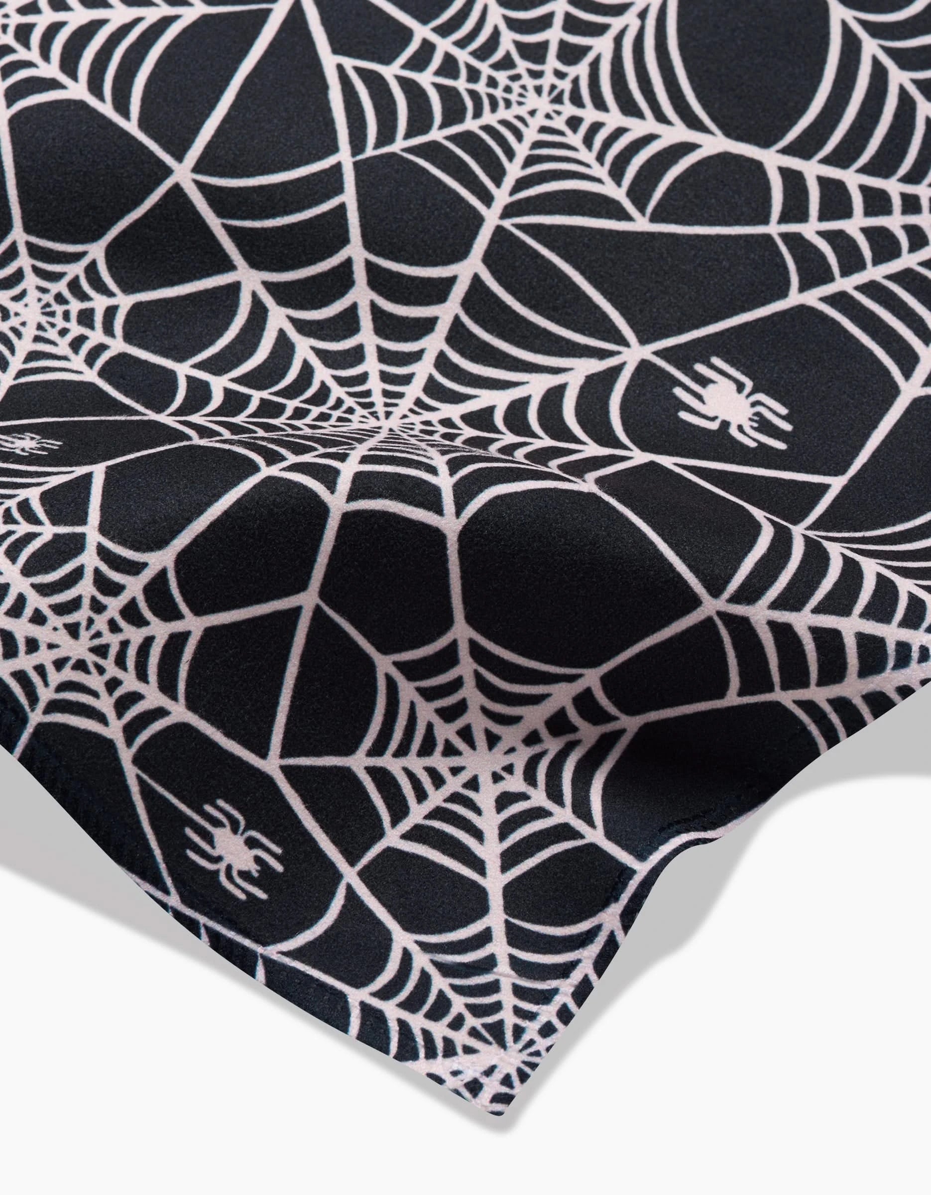 A close-up of Kayla Anns Booos napkins, black and eco-friendly, featuring a white spiderweb pattern with small white spiders throughout the design.