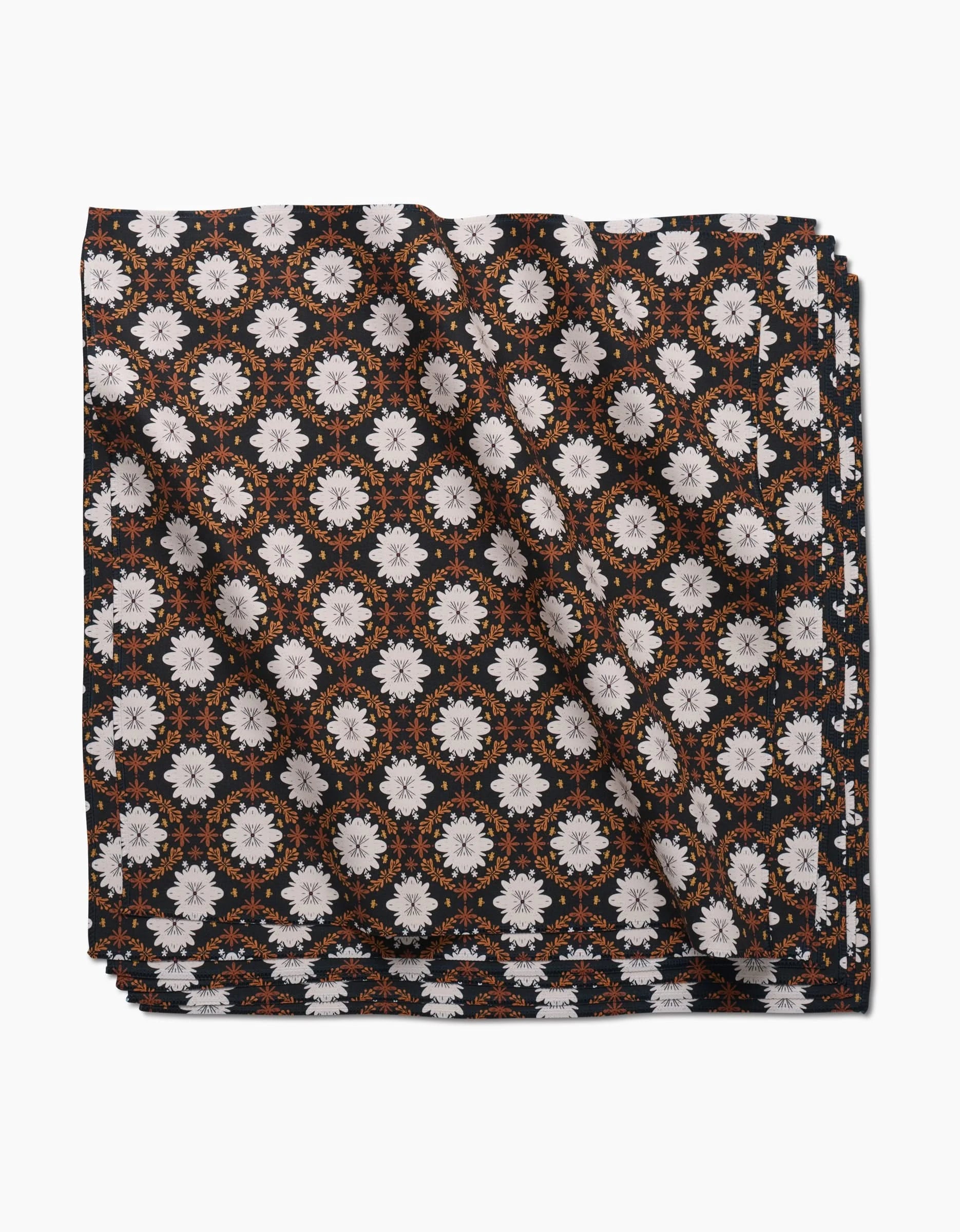 The Danelys Sidron Botanical Mosaic pocket square, crafted from recycled Geosuede, displays white and orange floral motifs on black, shown neatly folded against a white background.