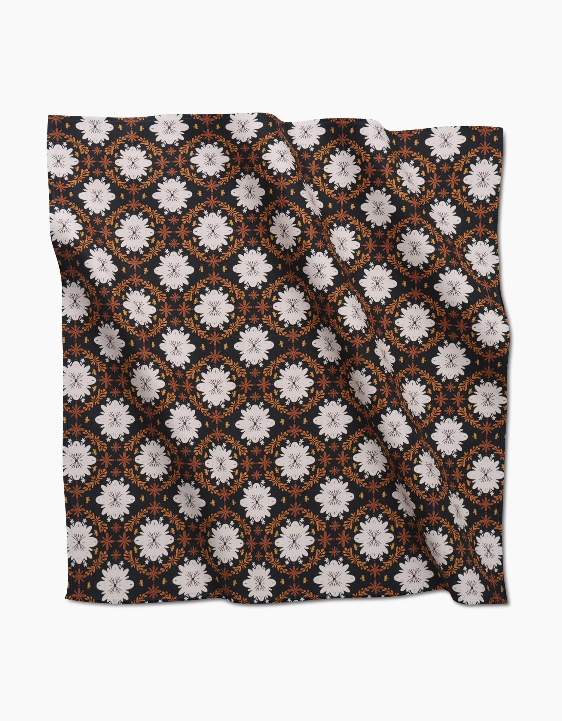 The Botanical Mosaic Dinner Napkin by Danelys Sidron features a black Geosuede square with white floral patterns, orange circular details, and a slightly wrinkled finish for a relaxed look.