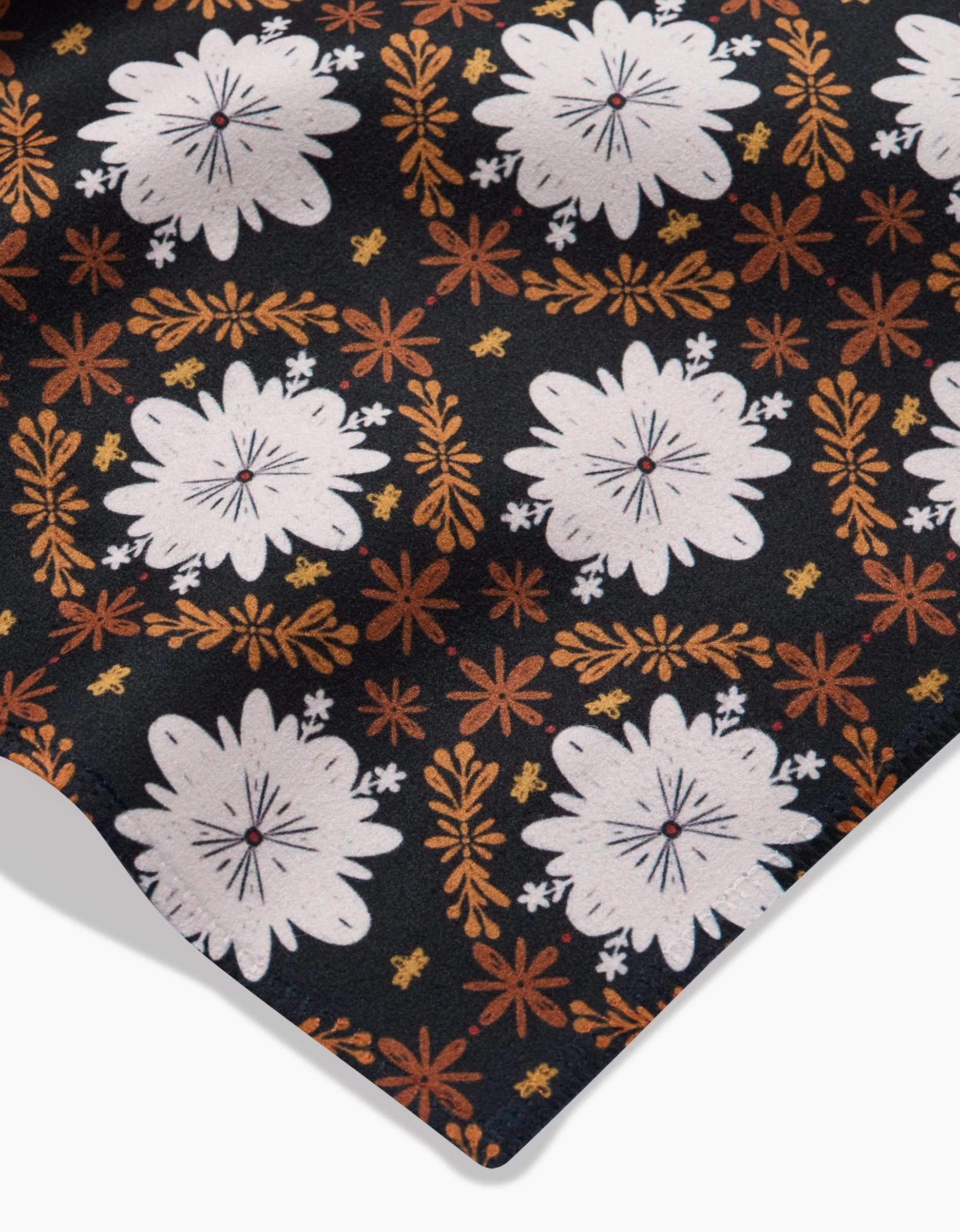 A close-up of Danelys Sidron’s Botanical Mosaic shows Geosuede fabric with large white florals and orange and yellow motifs on black, ideal for eco-friendly Dinner Napkins made from recycled materials. The fabric edge appears in the lower right corner.