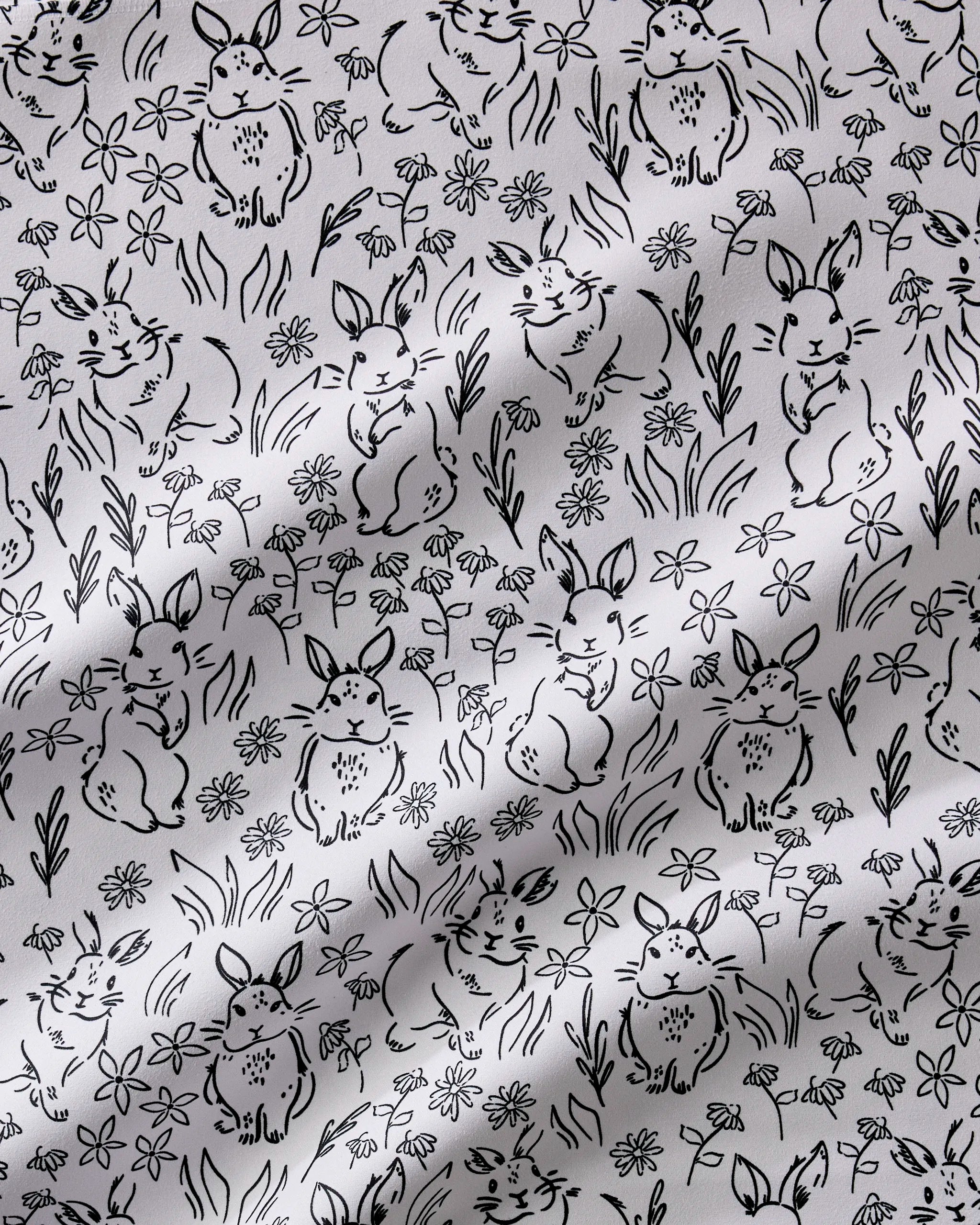 The Bunny Rabbit Garden dinner napkin set by Charlie Rowan Designs features black and white Geosuede fabric with hand-drawn bunnies in playful poses amid flowers and grass, adding a whimsical touch to your table.