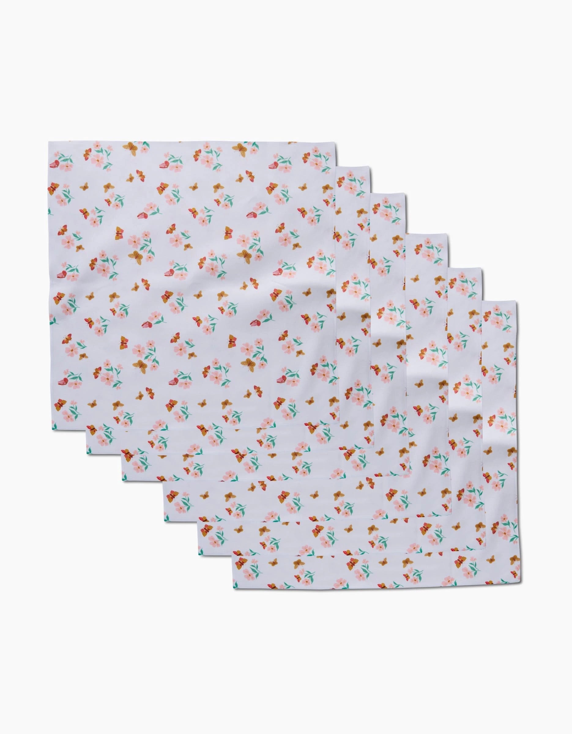 Six white Butterfly Garden Dinner Napkins by Danelys Sidron, made from recycled materials and featuring a small pink, orange, and green floral pattern, are arranged in a staggered row on a plain background.