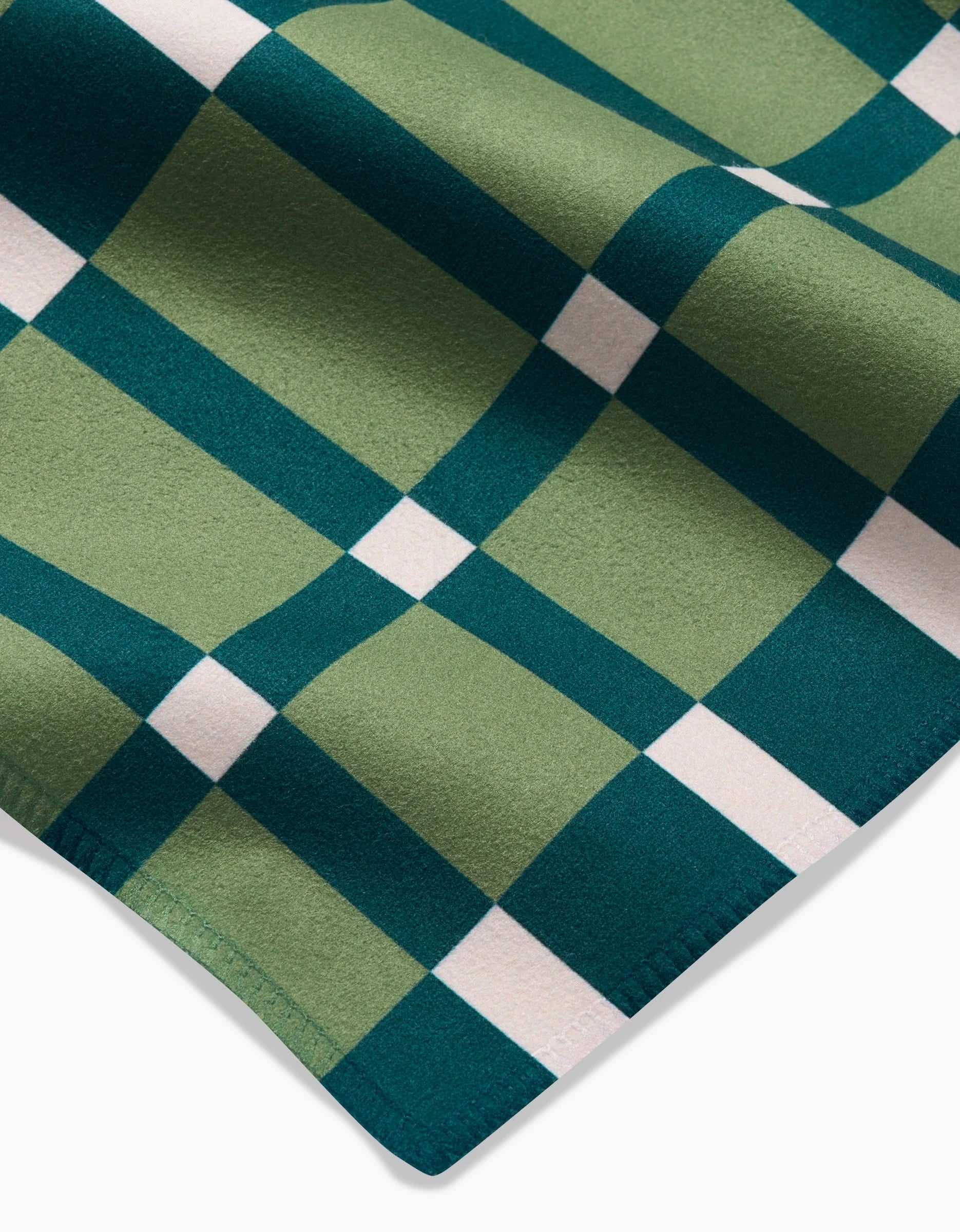 A close-up of Candy Plaid by Rebecca Woolbright shows green and dark teal checks with thin white grid lines. The soft Geosuede fabric, slightly folded at the edge, is ideal for an elegant recycled napkin set.