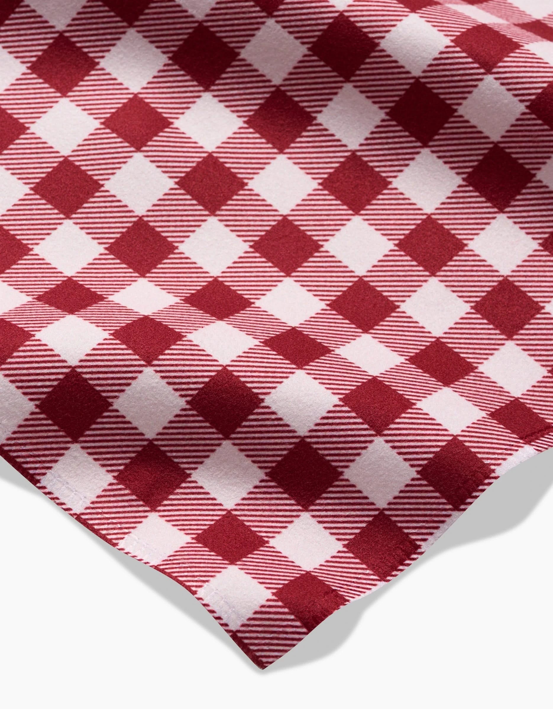 A close-up of the Aubrey Fairchild Christmas Gingham napkin shows its red and white diagonal checkered pattern with alternating solid and striped squares; the eco-friendly edge appears in the lower right corner.
