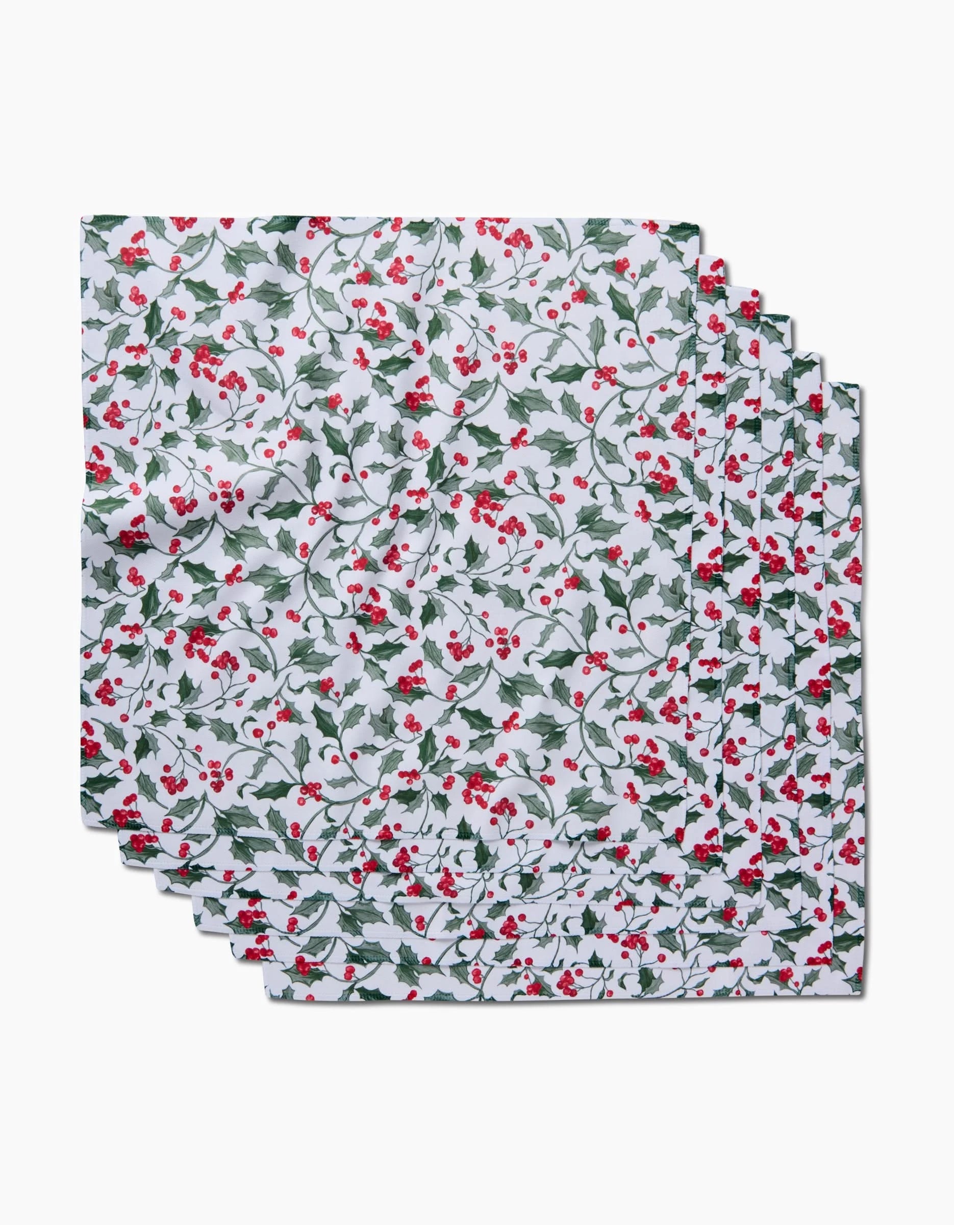 Six recycled Christmas Holly dinner napkins by Aubrey Fairchild, featuring red and green holly and berry patterns on white, arranged in a slightly overlapping stack.