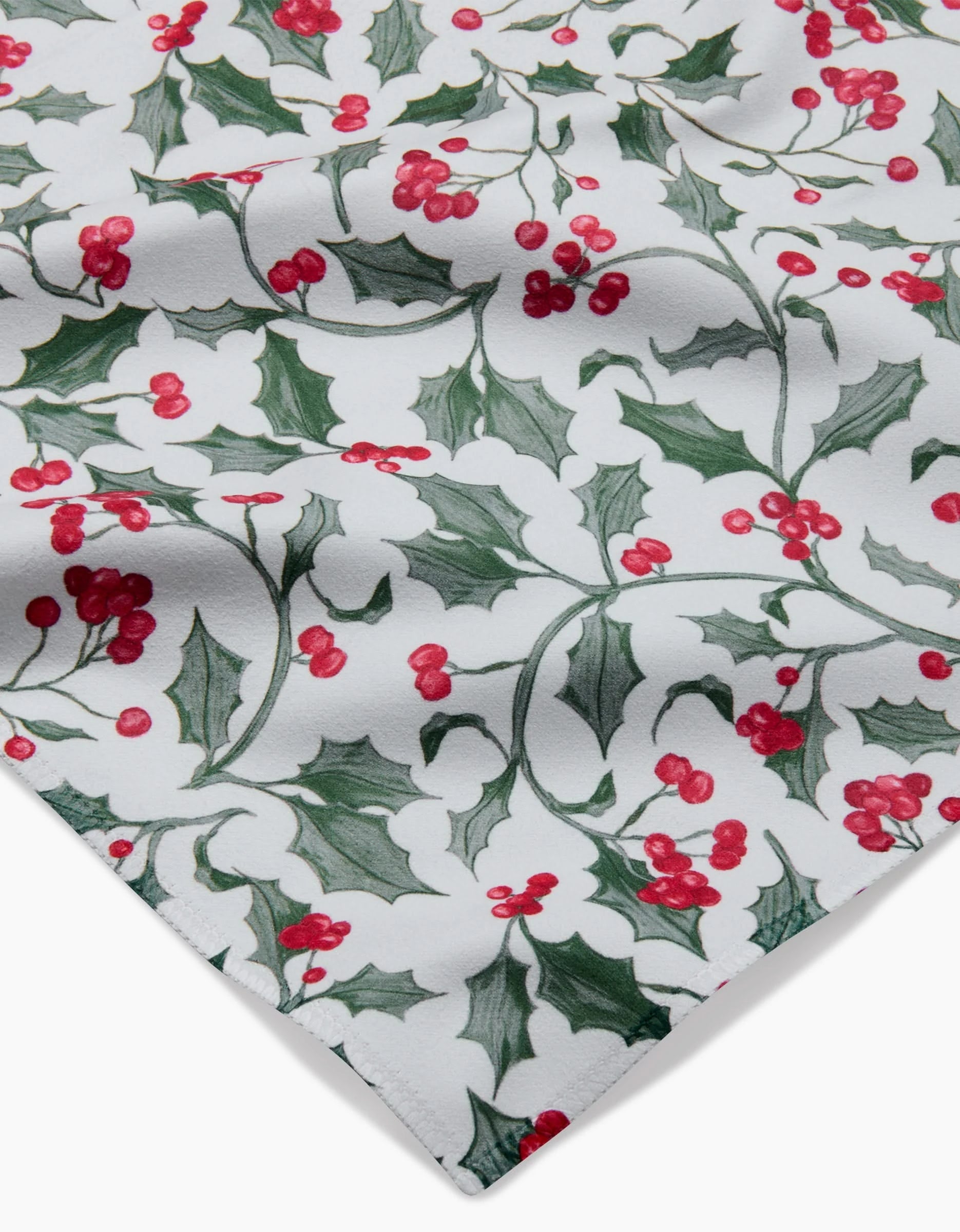 The Christmas Holly napkin by Aubrey Fairchild is a white absorbent cloth decorated with green holly leaves and red berry clusters, creating a classic holiday or Christmas look.