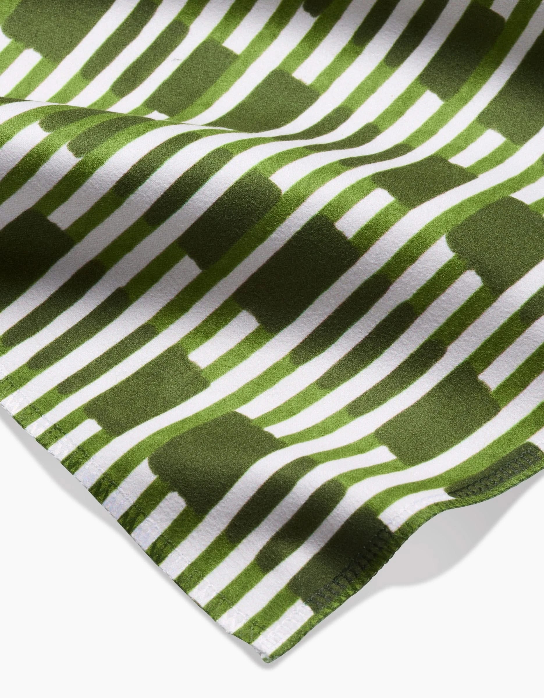 A close-up of GEOMETRY’s Clover Stripe shows its green and white geometric pattern in Geosuede fabric, with horizontal stripes and rectangles, softly draped and gently folded at the edge.