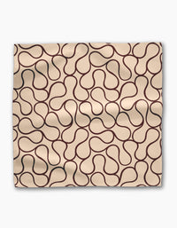 The Coffee Swirl Dinner Napkin Set by Gerdadzy features beige Geosuede fabric with smooth texture and subtle folds, accented by a modern abstract pattern of brown swirling lines for an organic look.