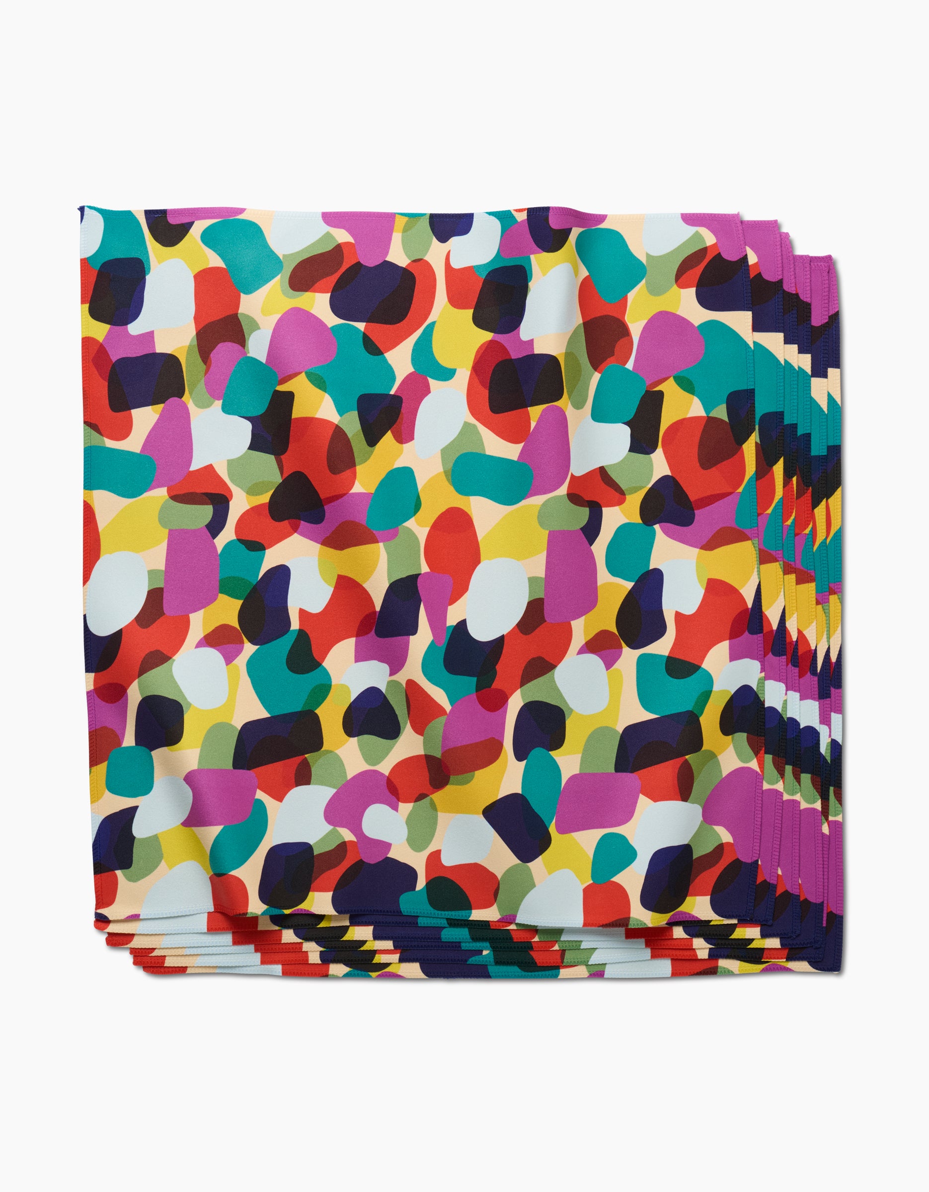 The GEOMETRY Colorful Pebbles Dinner Napkin Set showcases an abstract, multicolored pattern on Geosuede fabric, featuring red, yellow, green, purple, black, and white shapes scattered on a crisp white background.