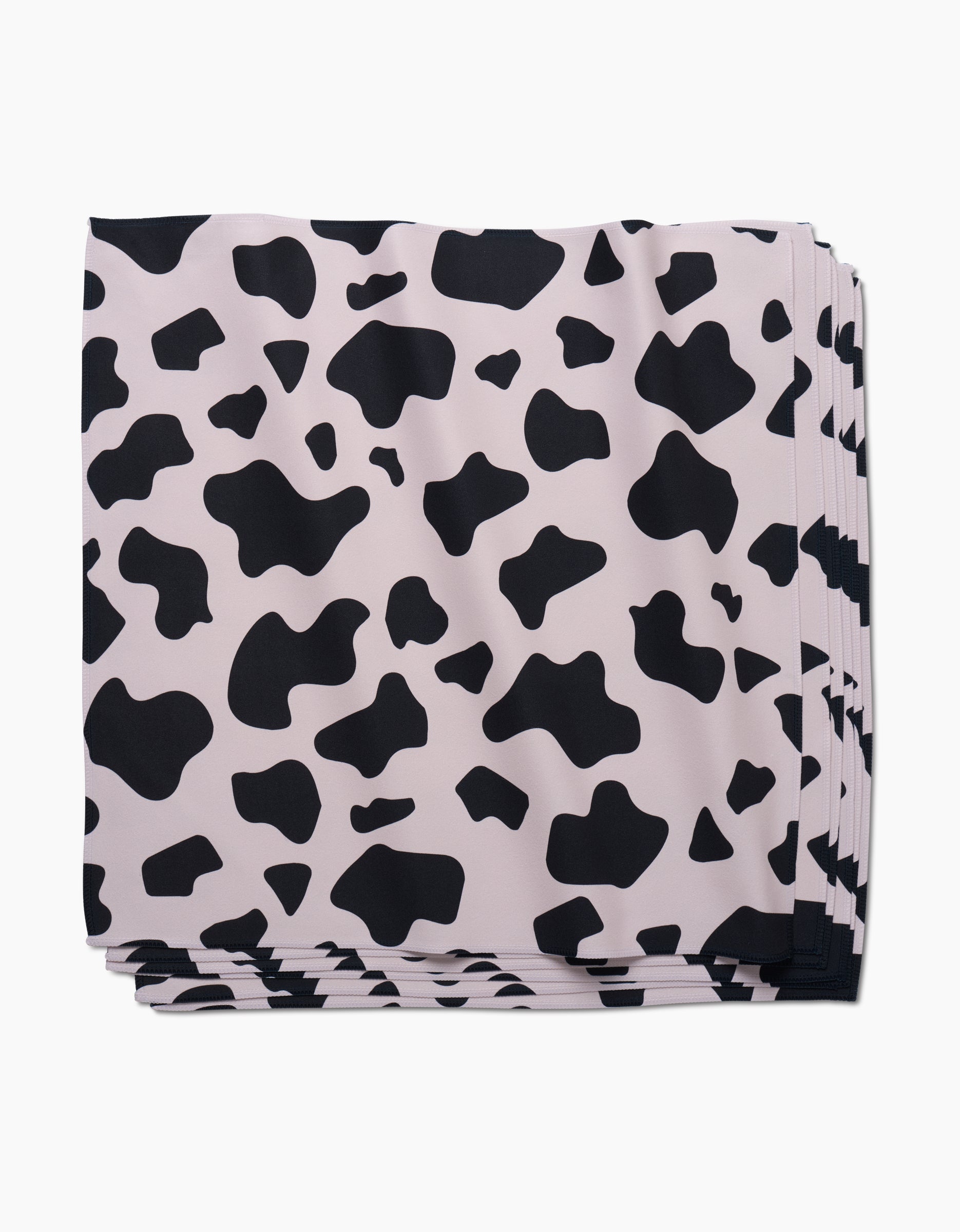 A stack of GEOMETRYs Cow Print Black Dinner Napkin Set, made from eco-friendly Geosuede fabric and featuring an irregular black and white cow print pattern.