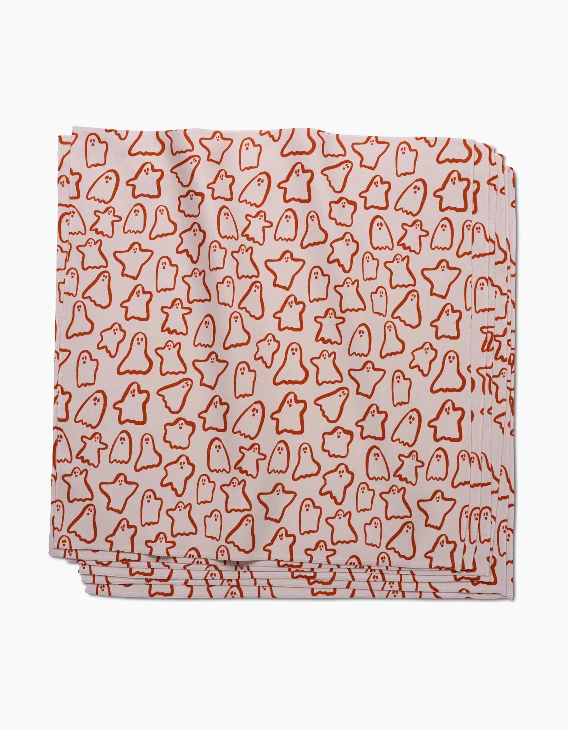 The Cute Ghosts dinner napkin set by Kayla Ann features folded white geosuede fabric with a playful pattern of small orange ghost illustrations scattered across the surface.