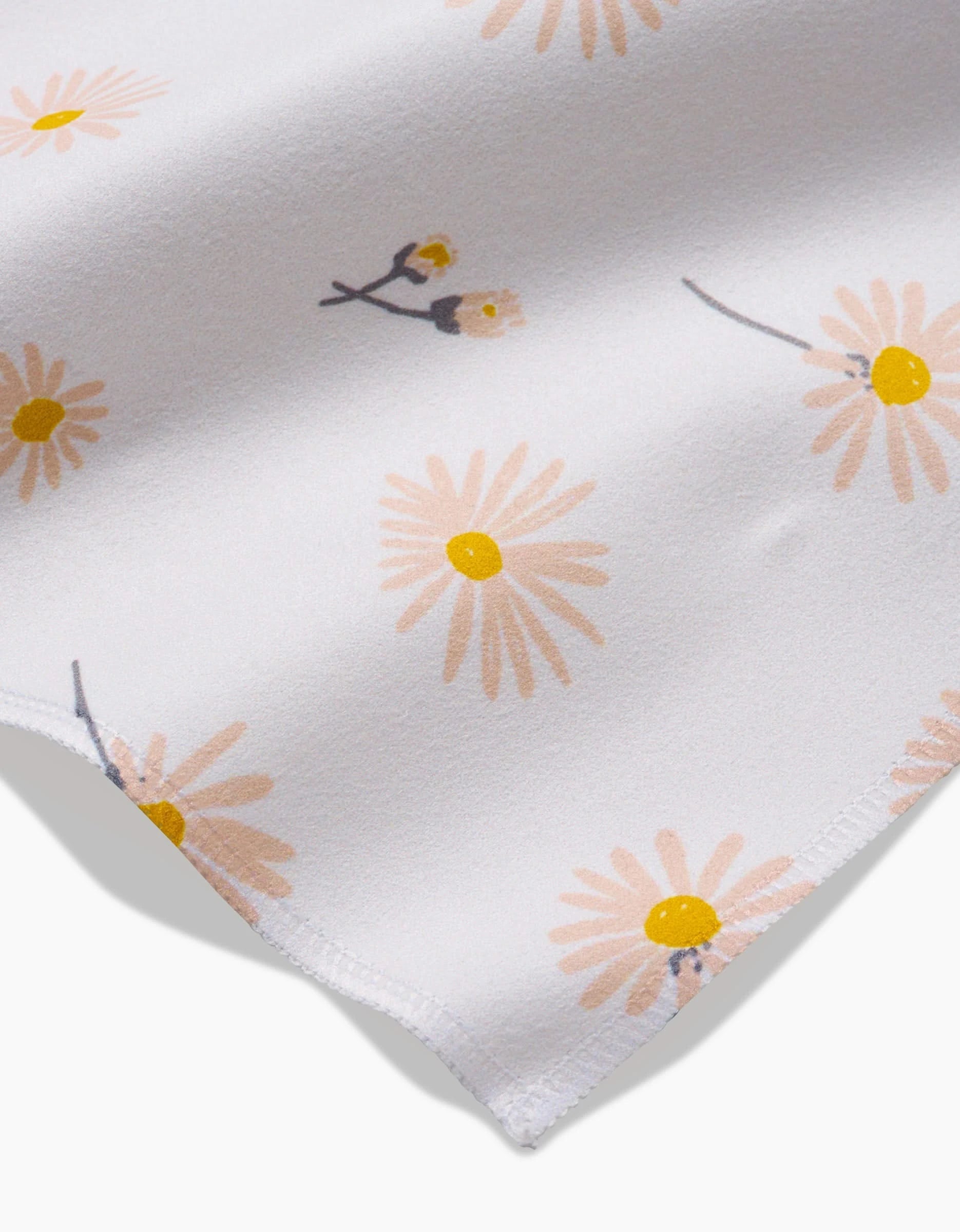 A close-up of the Daisy Dust Dinner Napkin by Hufton Studio, made from soft Geosuede fabric with yellow and peach daisy flowers, gray stems, stitched edge, and crafted from recycled materials.