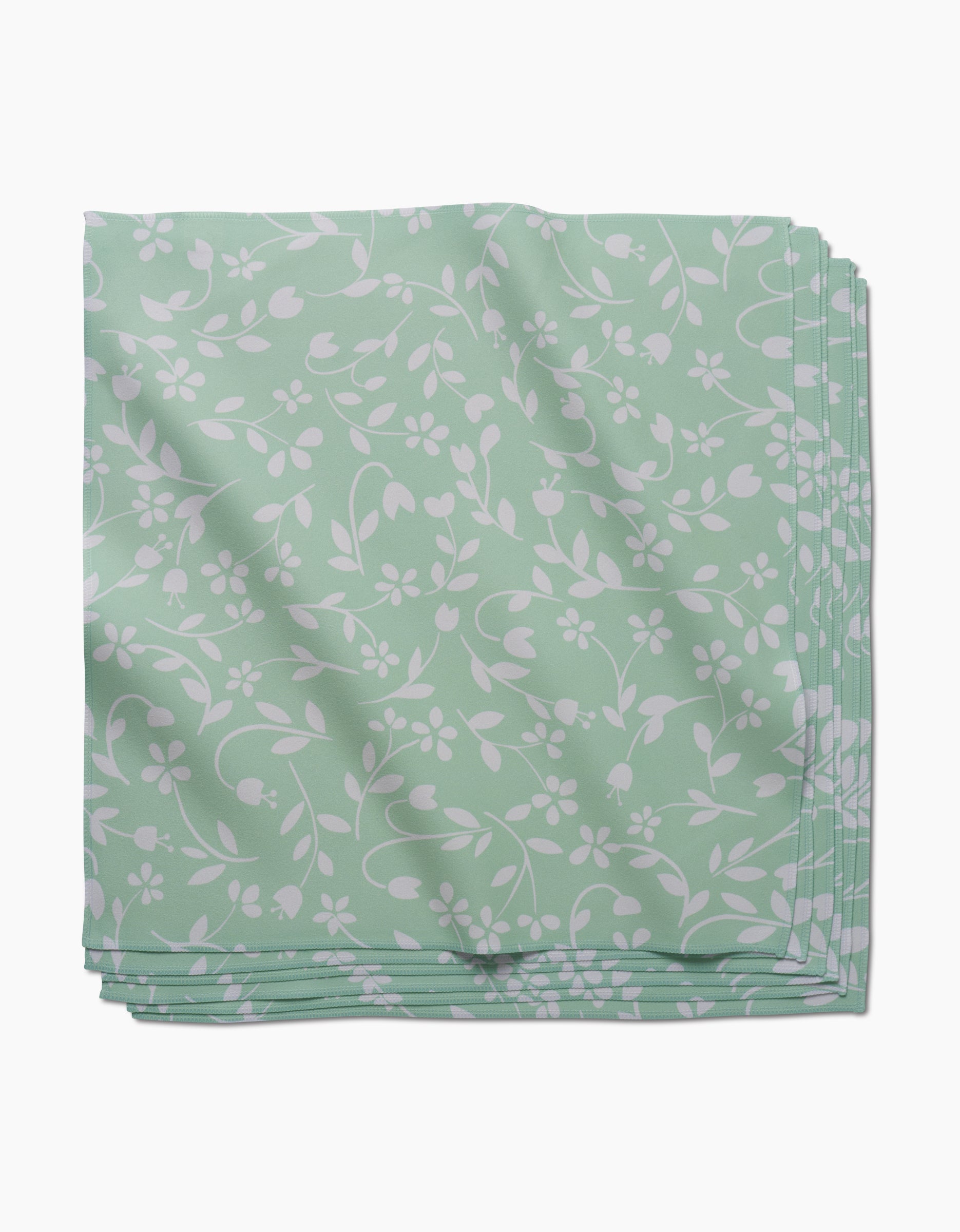 A neatly folded stack of GEOMETRY Dandy light green absorbent cloth napkins with a white floral and vine pattern, displayed on a white background.