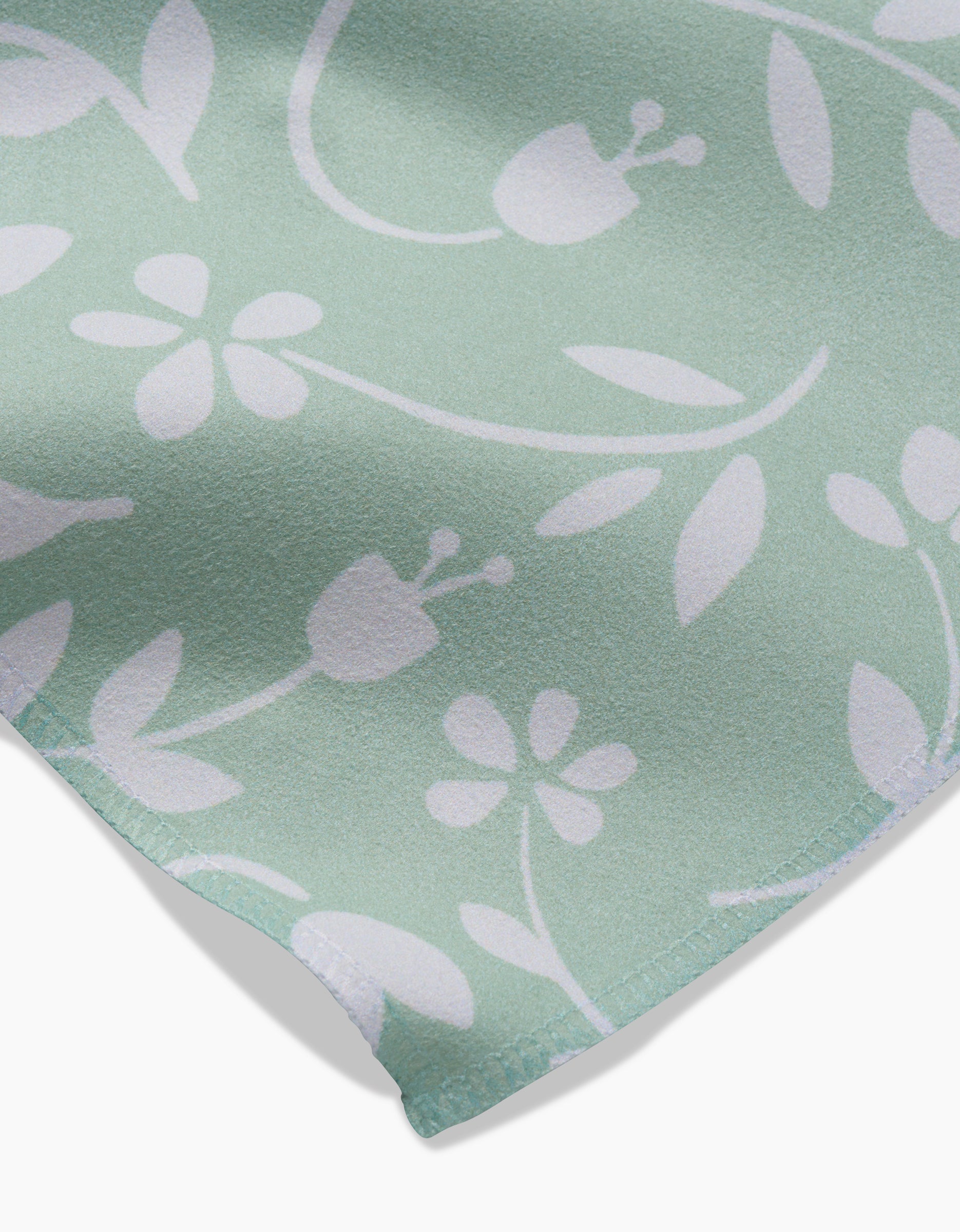 A close-up of the GEOMETRY Dandy dinner napkin set in light green, showcasing a white floral and leaf pattern with soft, curved shapes and visible edge stitching.