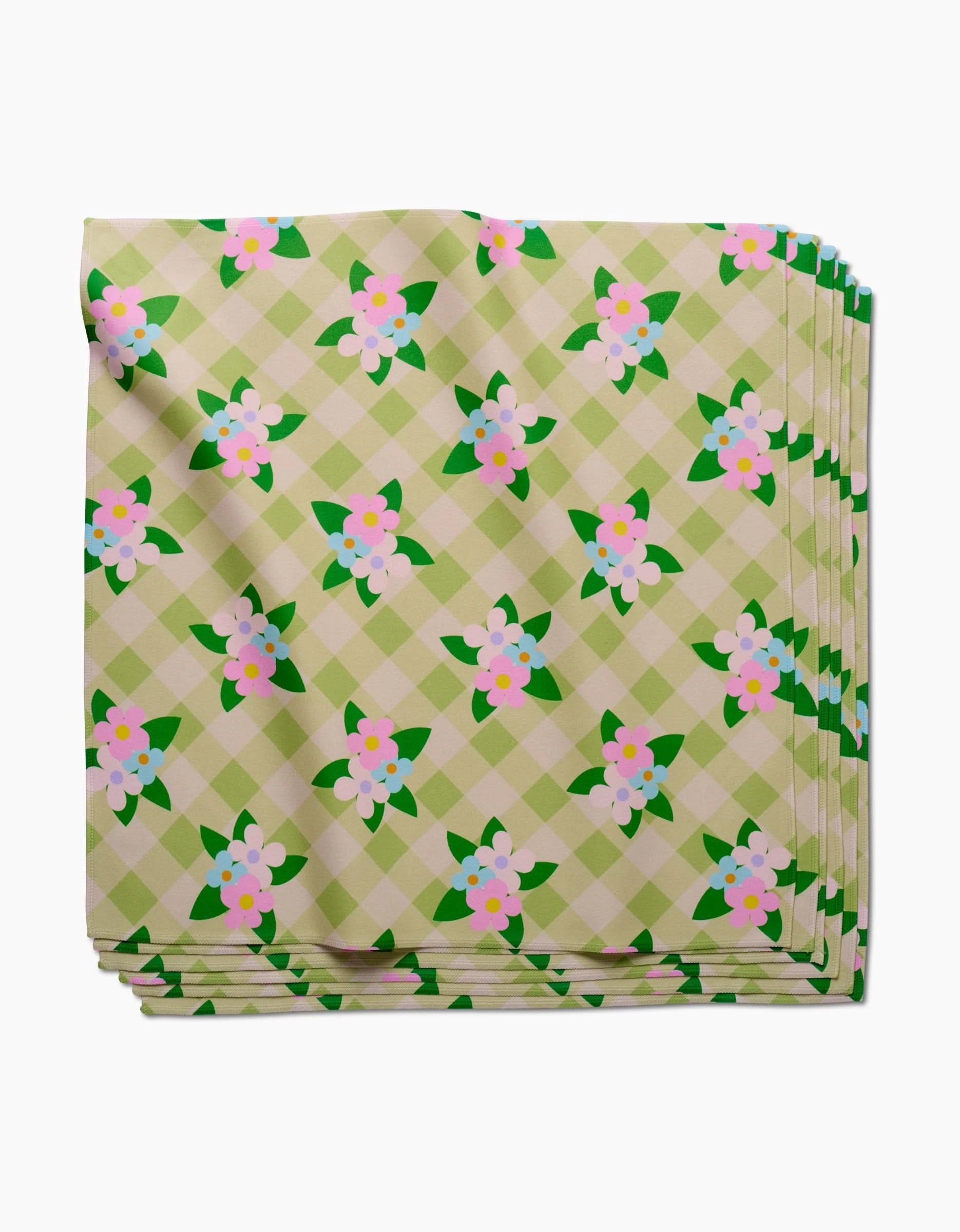 A folded stack of GEOMETRY’s Doting and Devoted Dinner Napkins, made from eco-friendly Geosuede fabric, features a green and cream checkered pattern with pink and white flowers and green leaves.