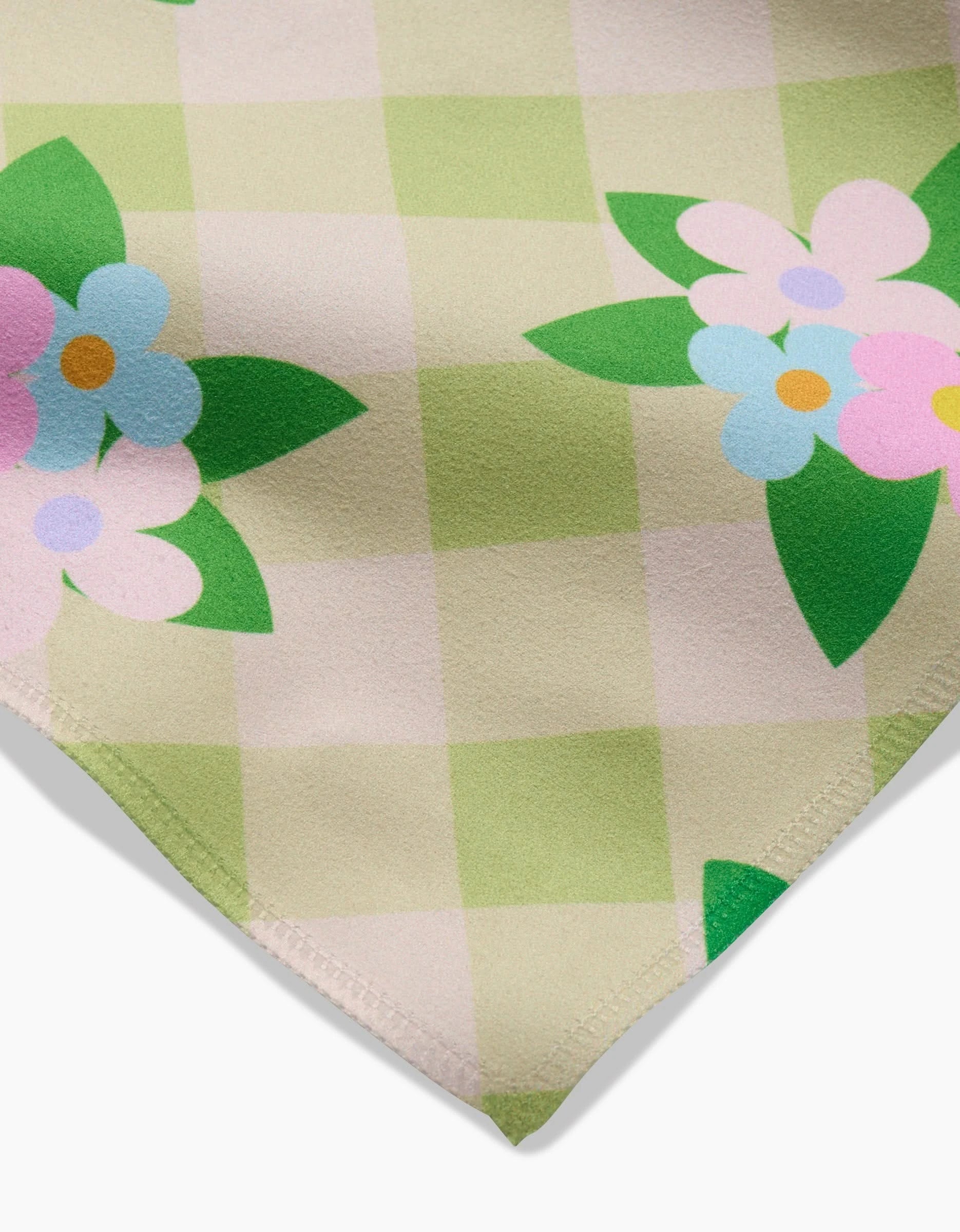 A close-up of GEOMETRYs Doting and Devoted Geosuede fabric in a green and beige checkerboard with colorful stylized flowers—an eco-friendly choice, ideal for dinner napkins.