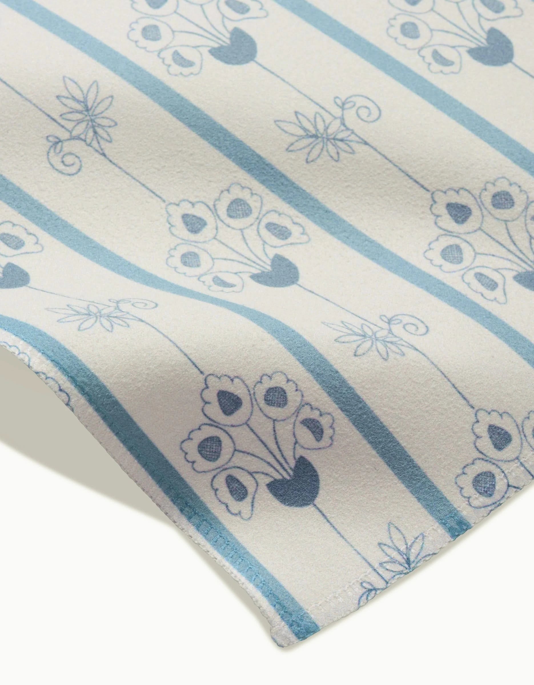 A close-up of GEOMETRY’s Ediths English Cottage absorbent cloth napkins, featuring blue and white vertical stripes and stylized floral designs with heart-shaped petals in vases.