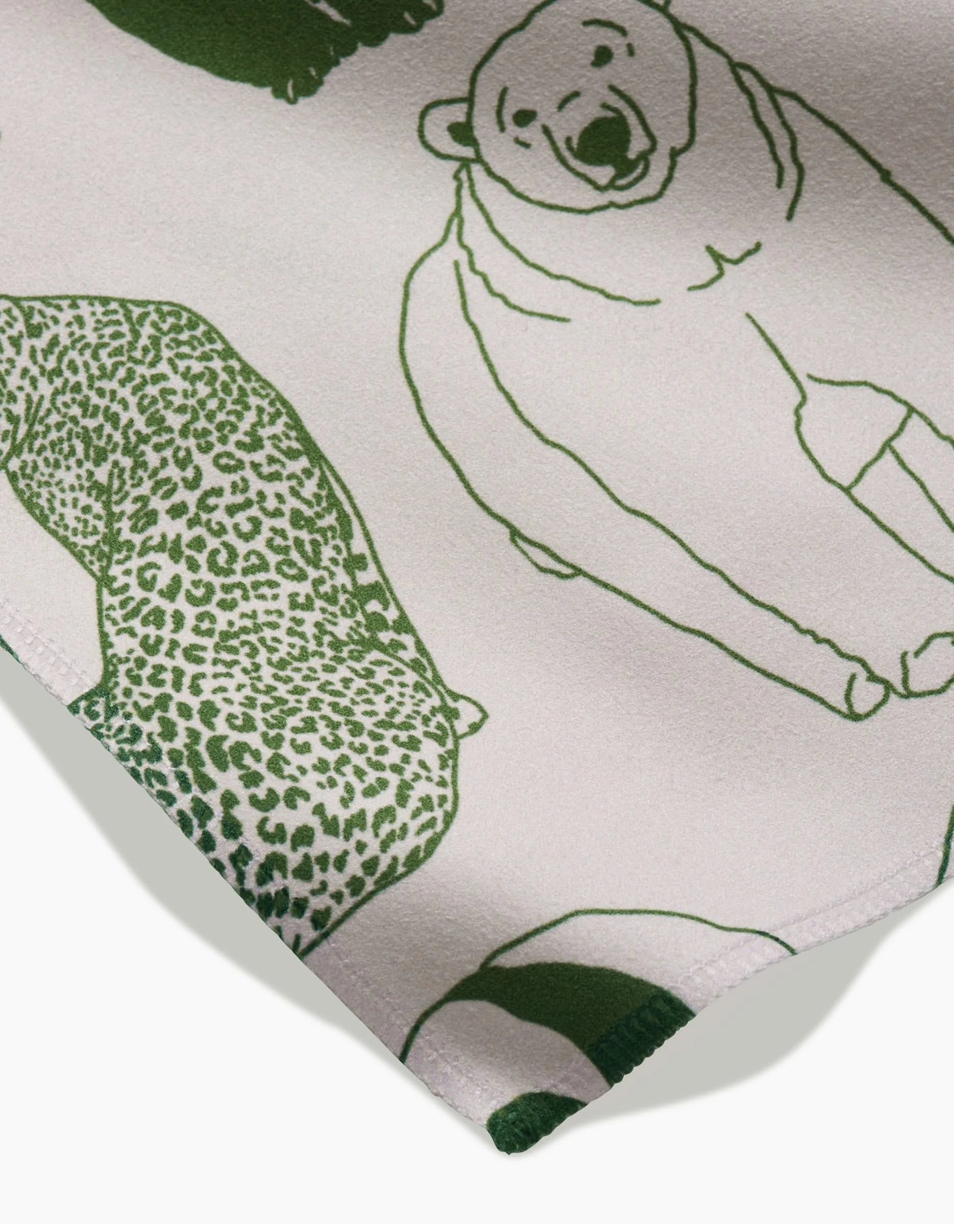 A close-up of GEOMETRYs Endangered Geosuede fabric, made from recycled materials, shows green animal line drawings—including a polar bear and leopard—on a light background, with the fabric edge visible in the lower corner.