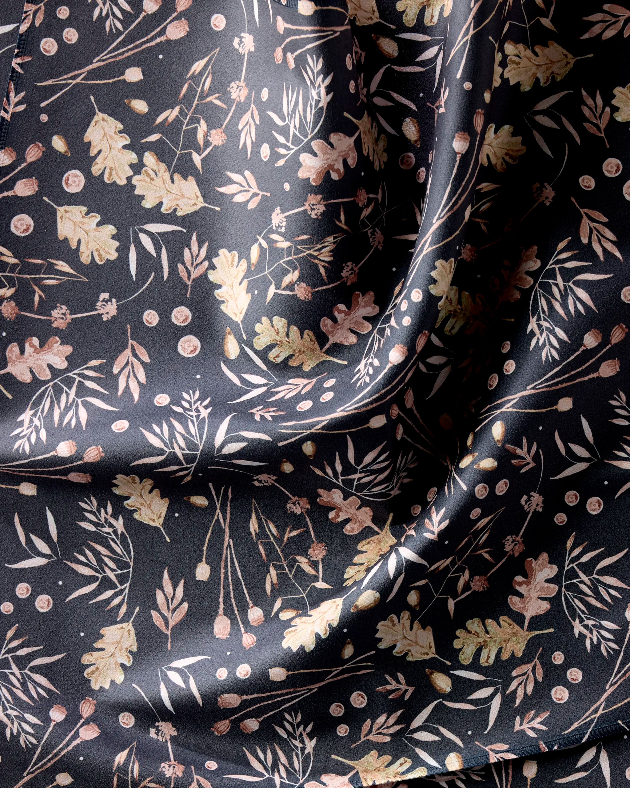 Fallen Oak by Katie O'Shea is a dark, silky napkin made from recycled fabric, featuring a pattern of light leaves, branches, and berries that catches the light to reveal its beautifully smooth texture.