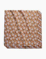 The Falling Acorns table linen by Charlie Rowan Designs features a brown background with a repeating white and black leaf pattern. This eco-friendly fabric is neatly folded and stacked, shown against a white backdrop.